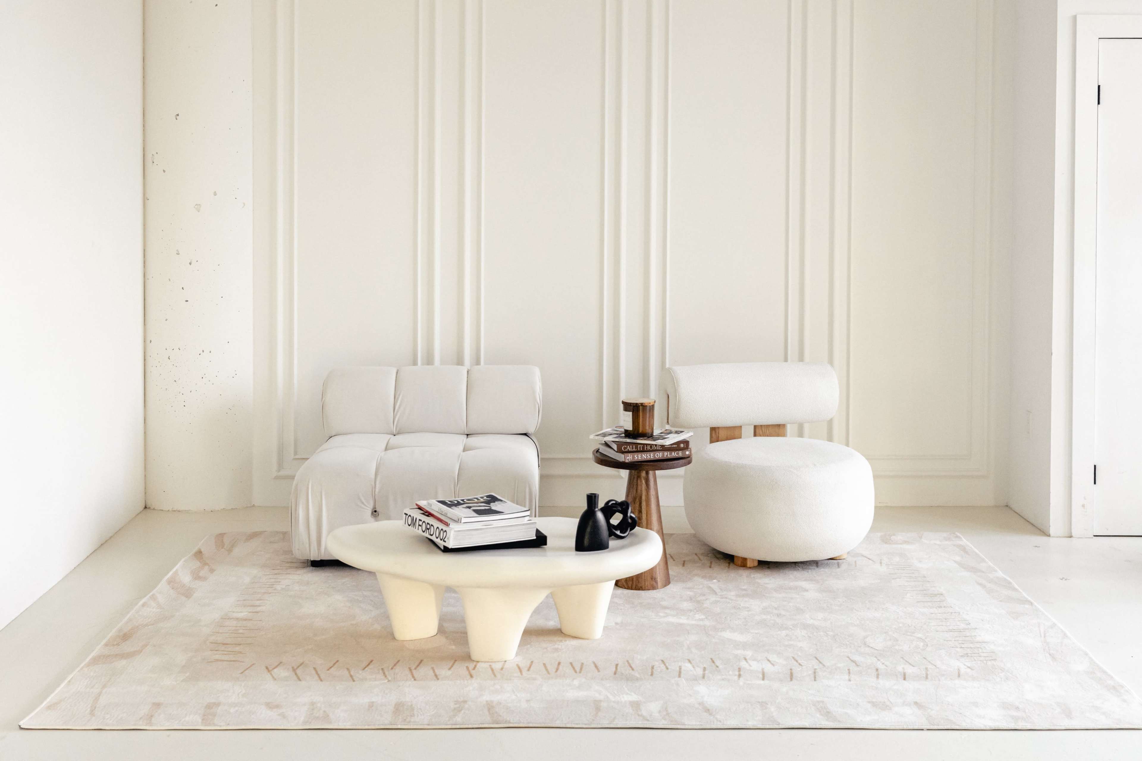 A minimalist seating area features a light-colored sofa and armchair, complemented by a circular coffee table and a textured area rug.