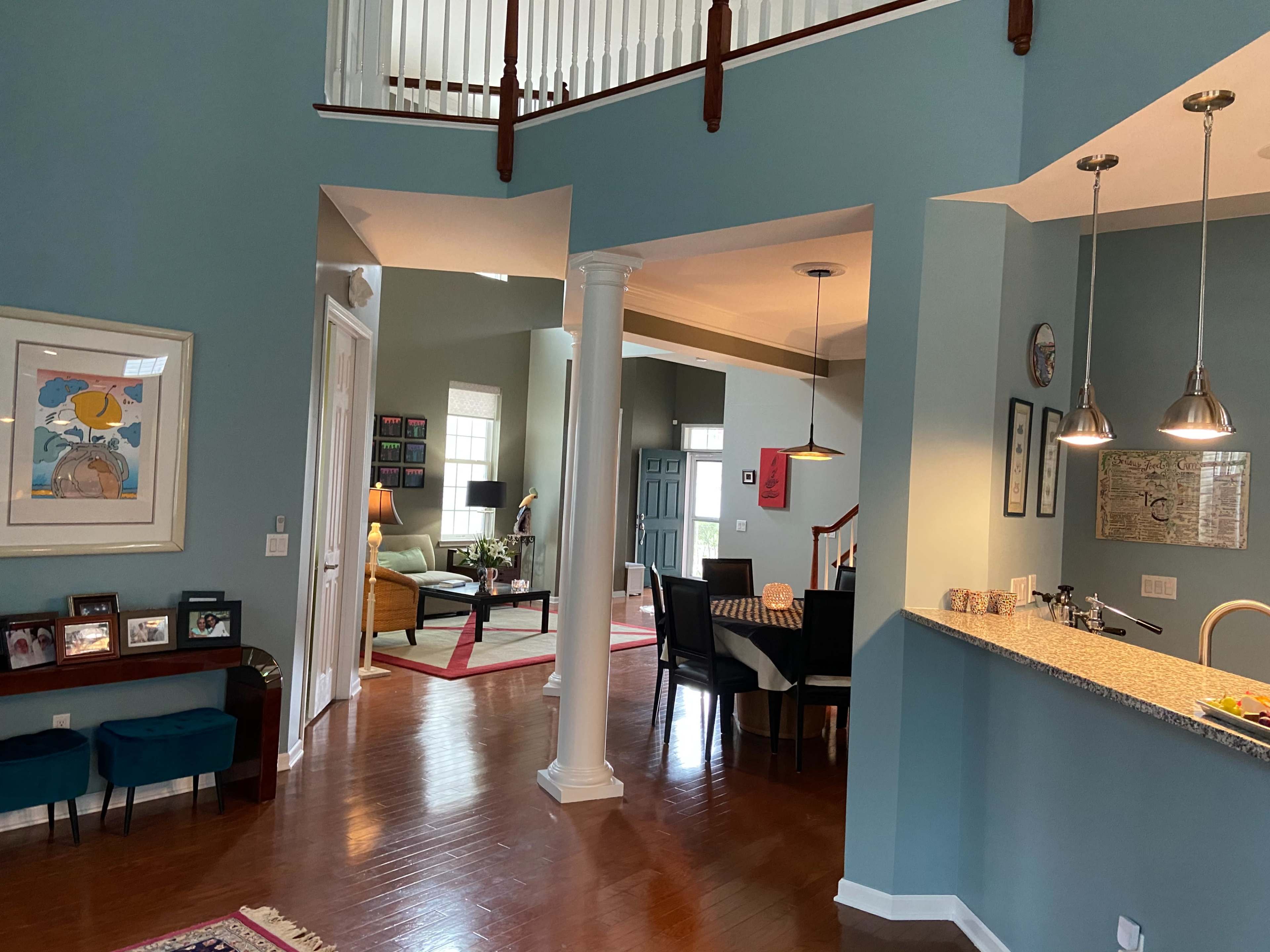 A spacious, modern living area with a kitchen bar, dining space, and a staircase visible in the background.