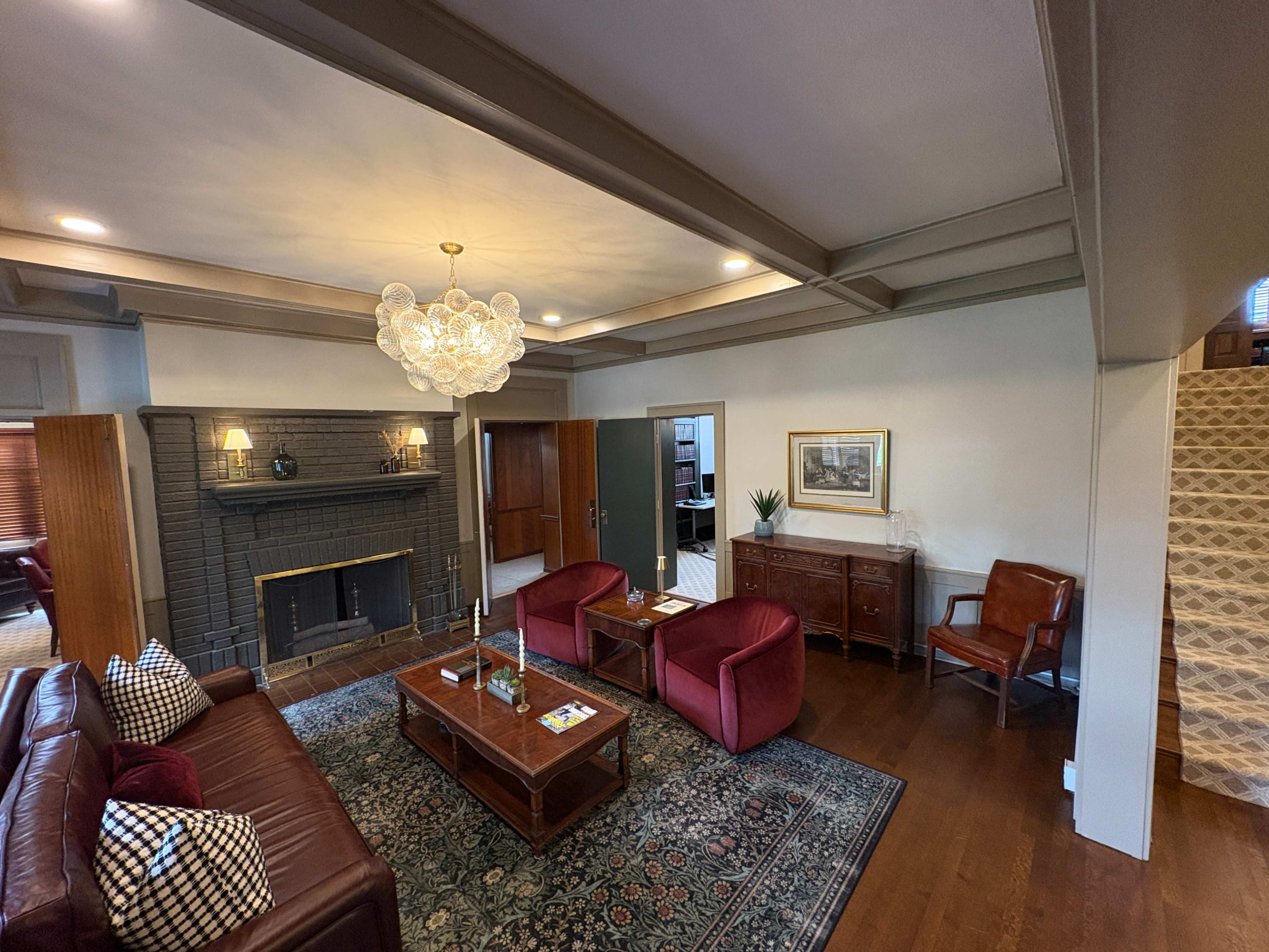 The image shows a living room with a dark fireplace, red furniture, a decorative chandelier, and a patterned area rug.
