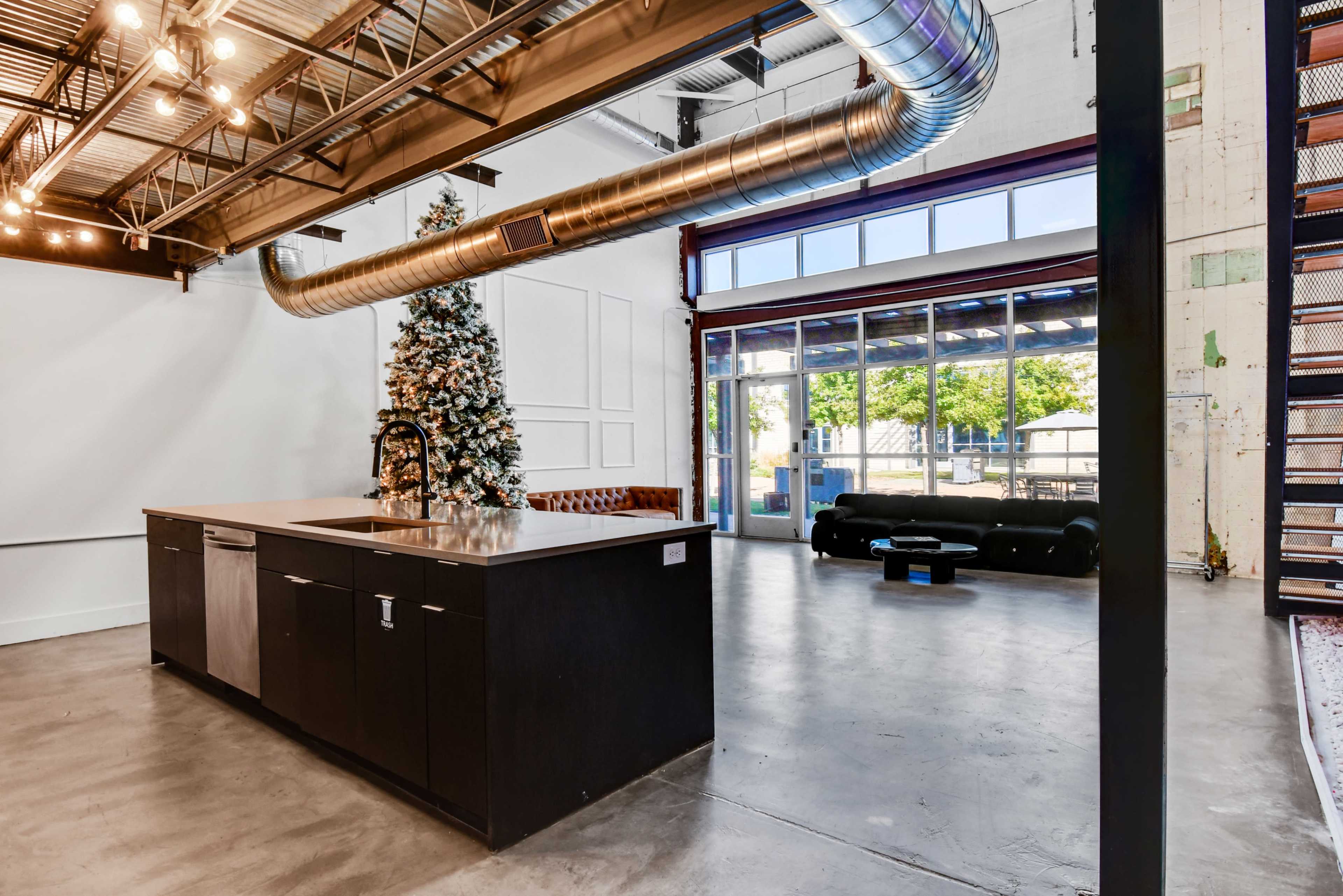 The image shows a modern, open-concept interior featuring a kitchen island with a large Christmas tree in the corner and large glass doors leading to an outdoor space.