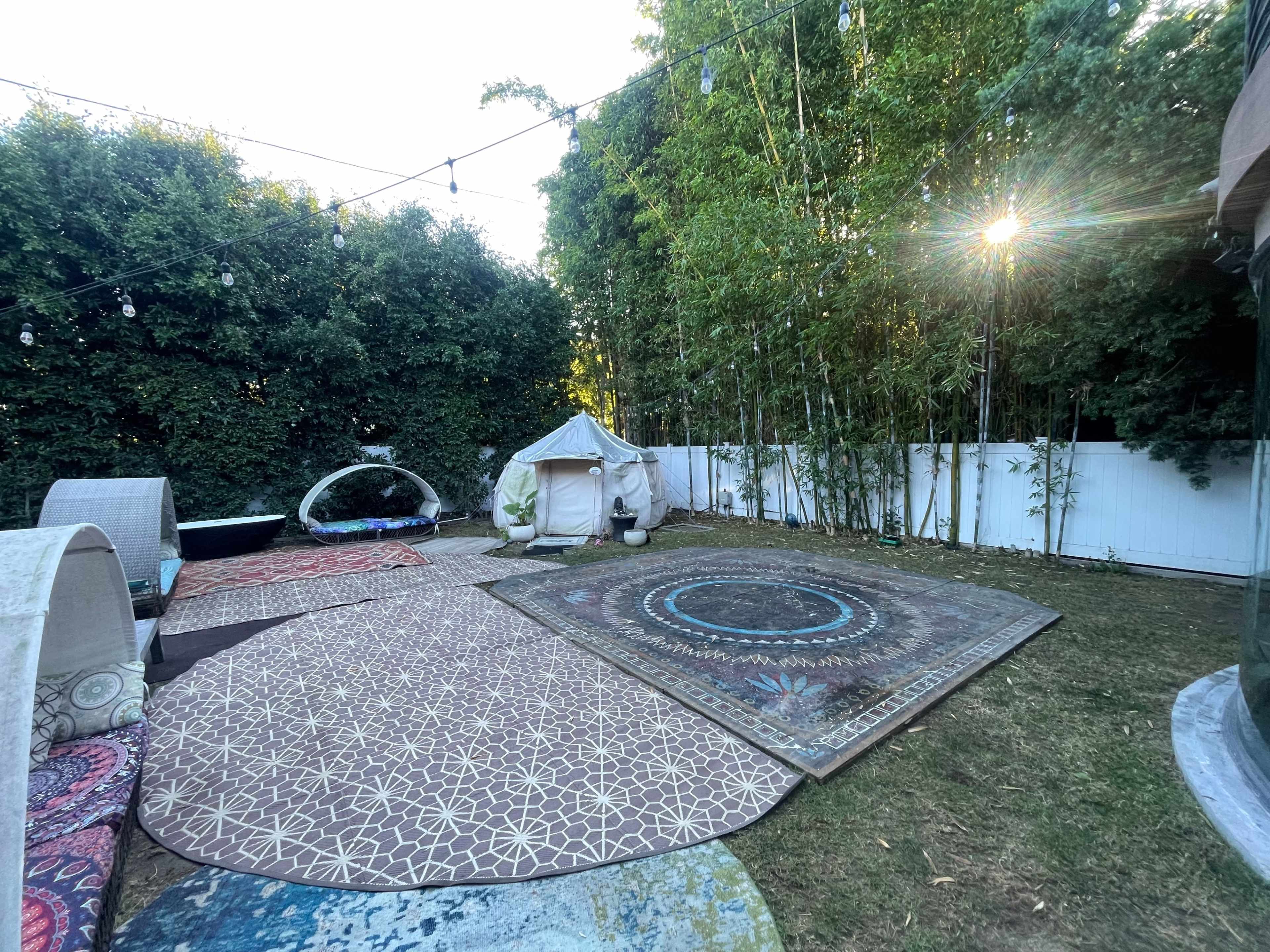 A landscaped backyard with multiple decorative rugs, a tent structure, and tall green hedges surrounding the area.