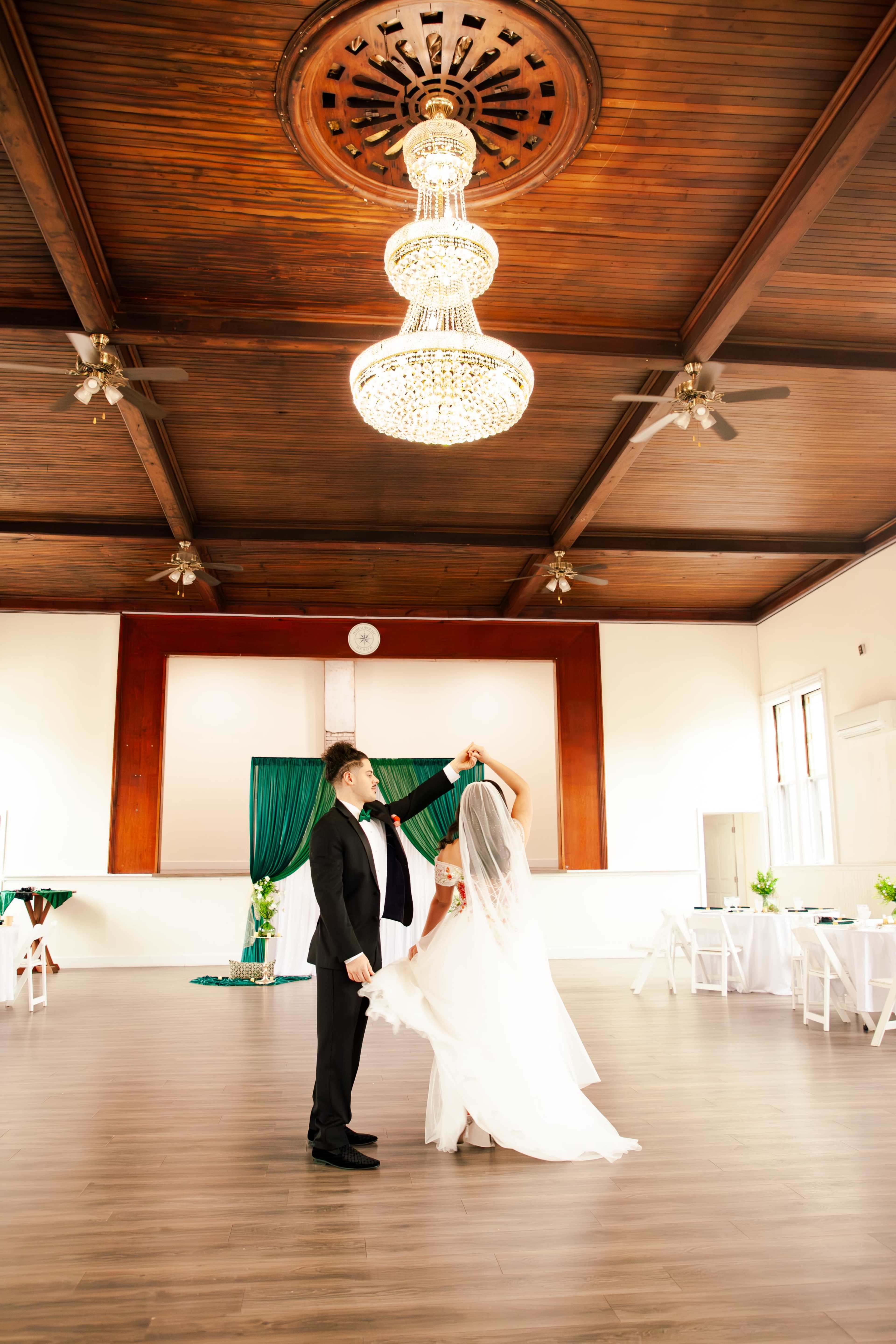 A couple dances together under a chandelier in a spacious, elegantly decorated indoor venue.