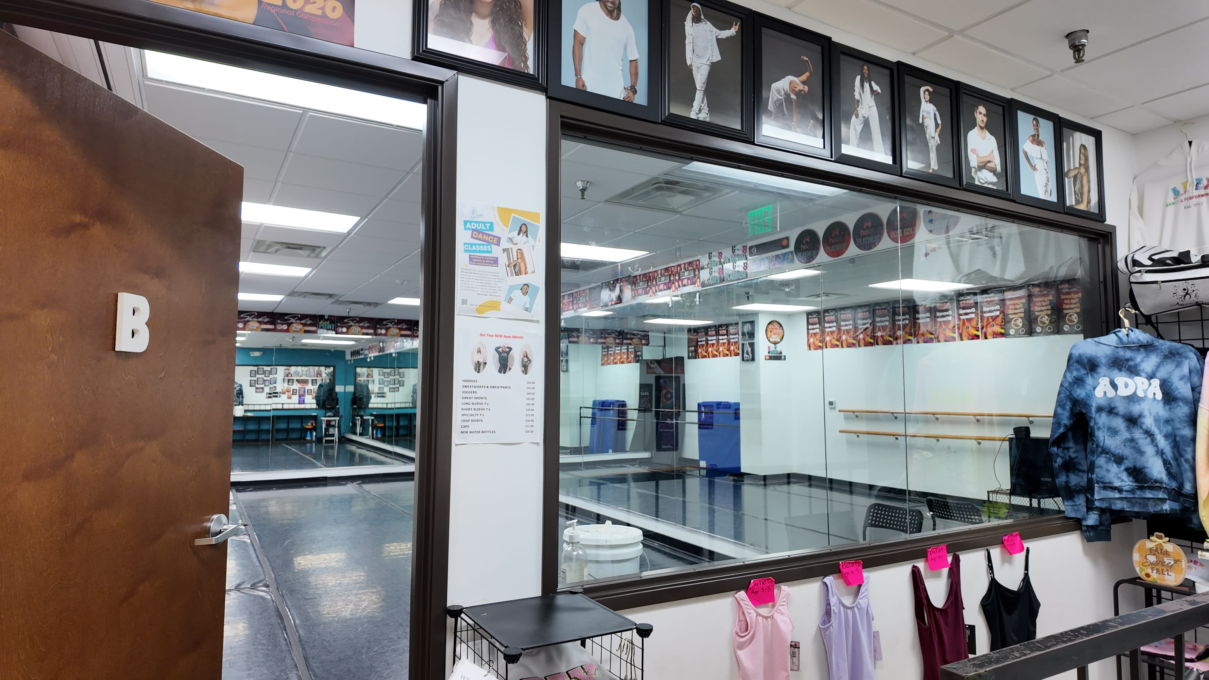 The image shows a dance studio visible through a glass wall, featuring ballet bars and posters of dancers on the walls.