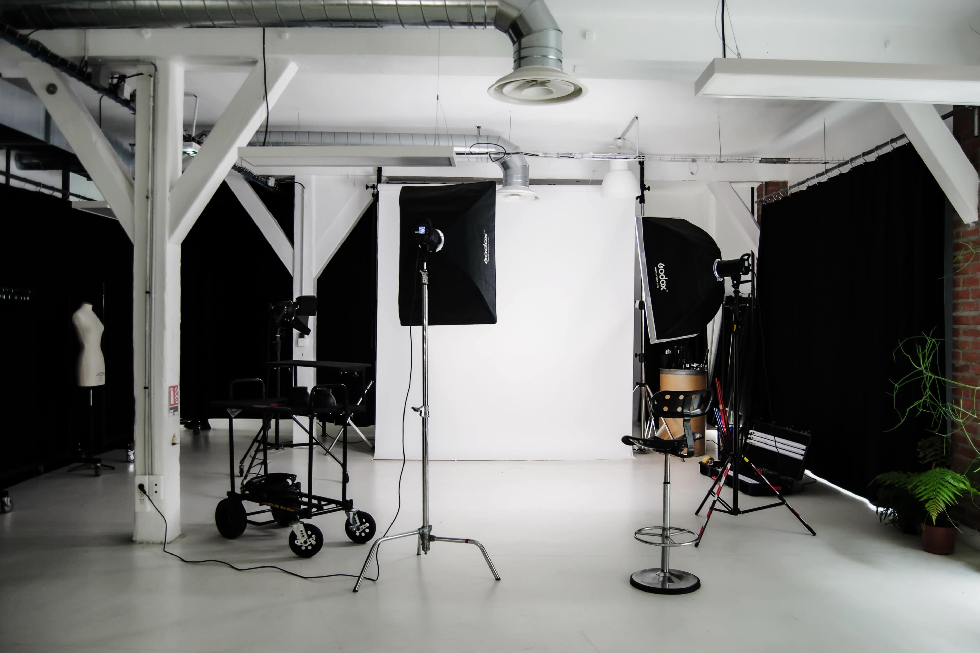 The image shows a photography studio equipped with lighting setups and a backdrop against a white wall.