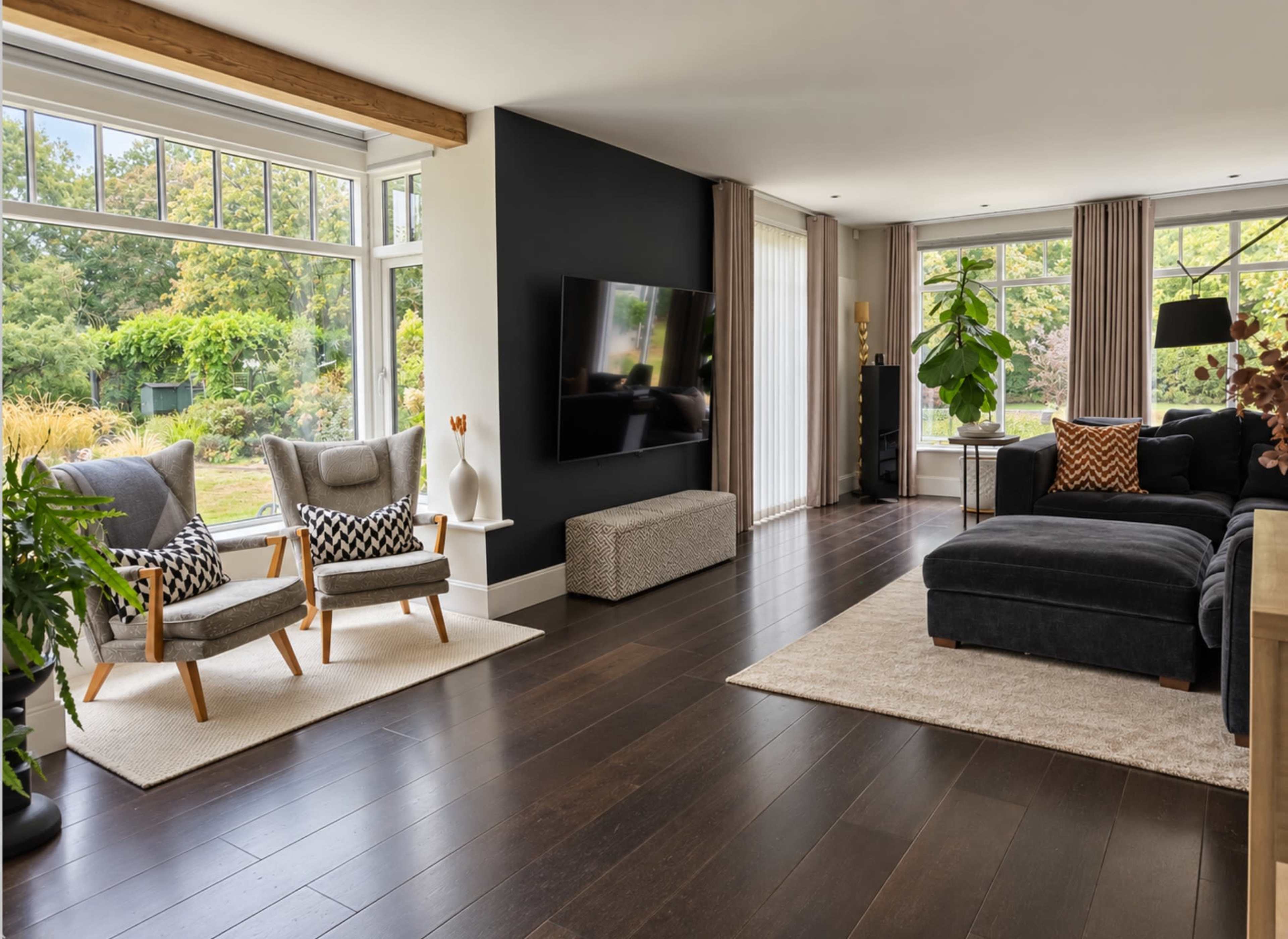 The image shows a modern living room with large windows, a sectional couch, two armchairs, and a flat-screen TV mounted on the wall.