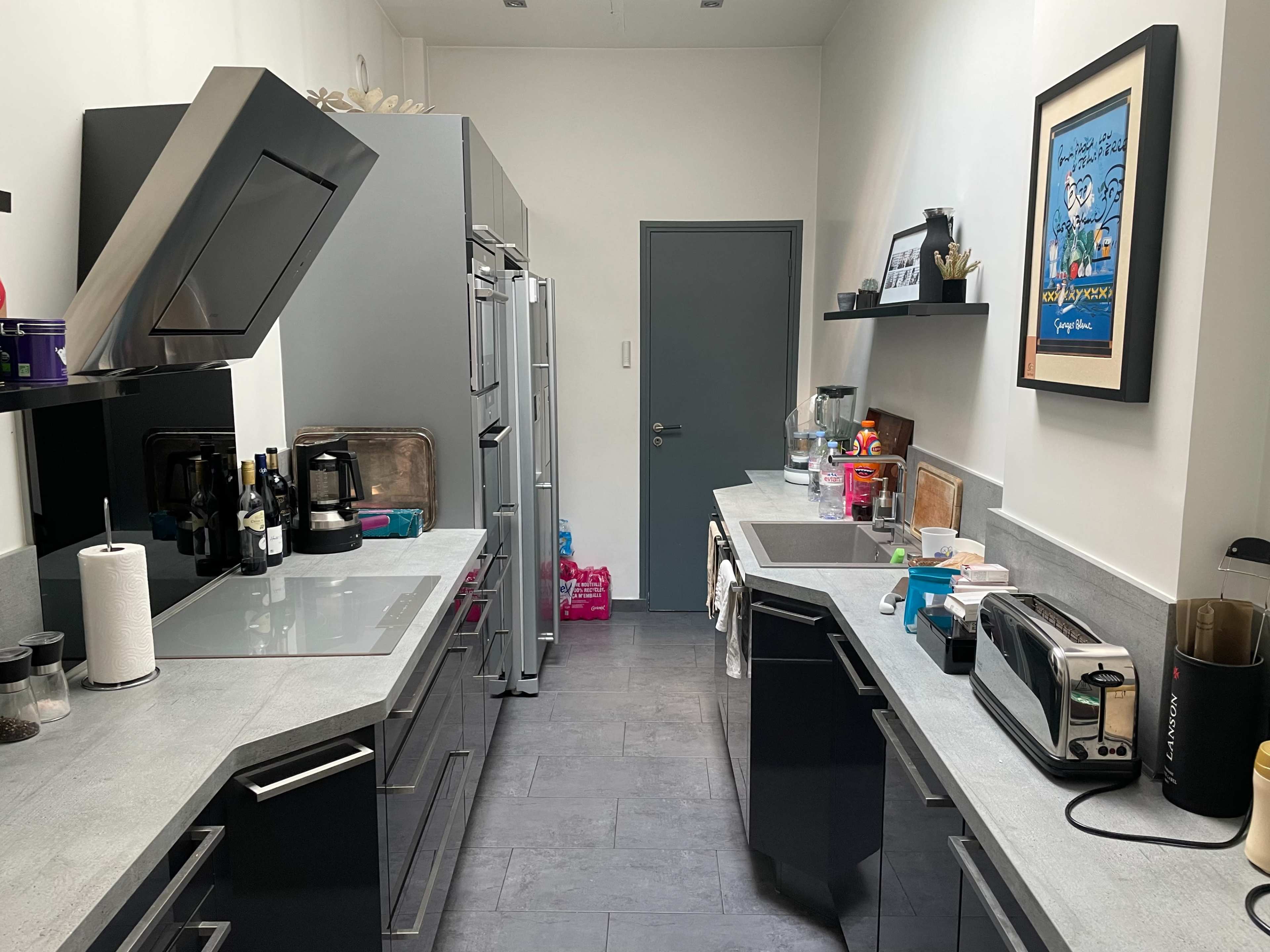 A modern kitchen with gray cabinets, a double sink, and various appliances arranged along the countertops.