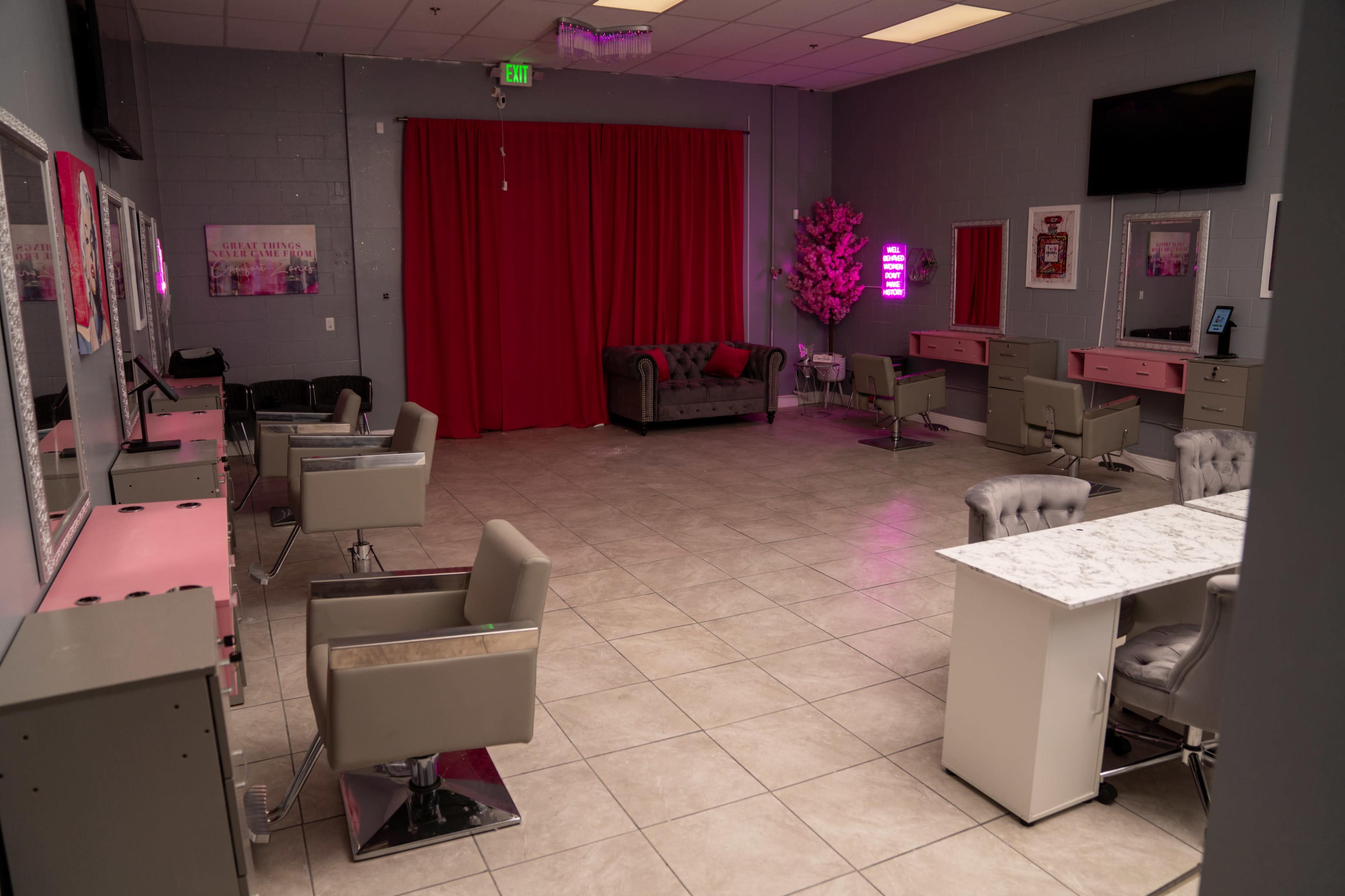 A beauty salon interior featuring several hair styling stations, a waiting area with a couch, and decorative elements including a red curtain and artificial plant.