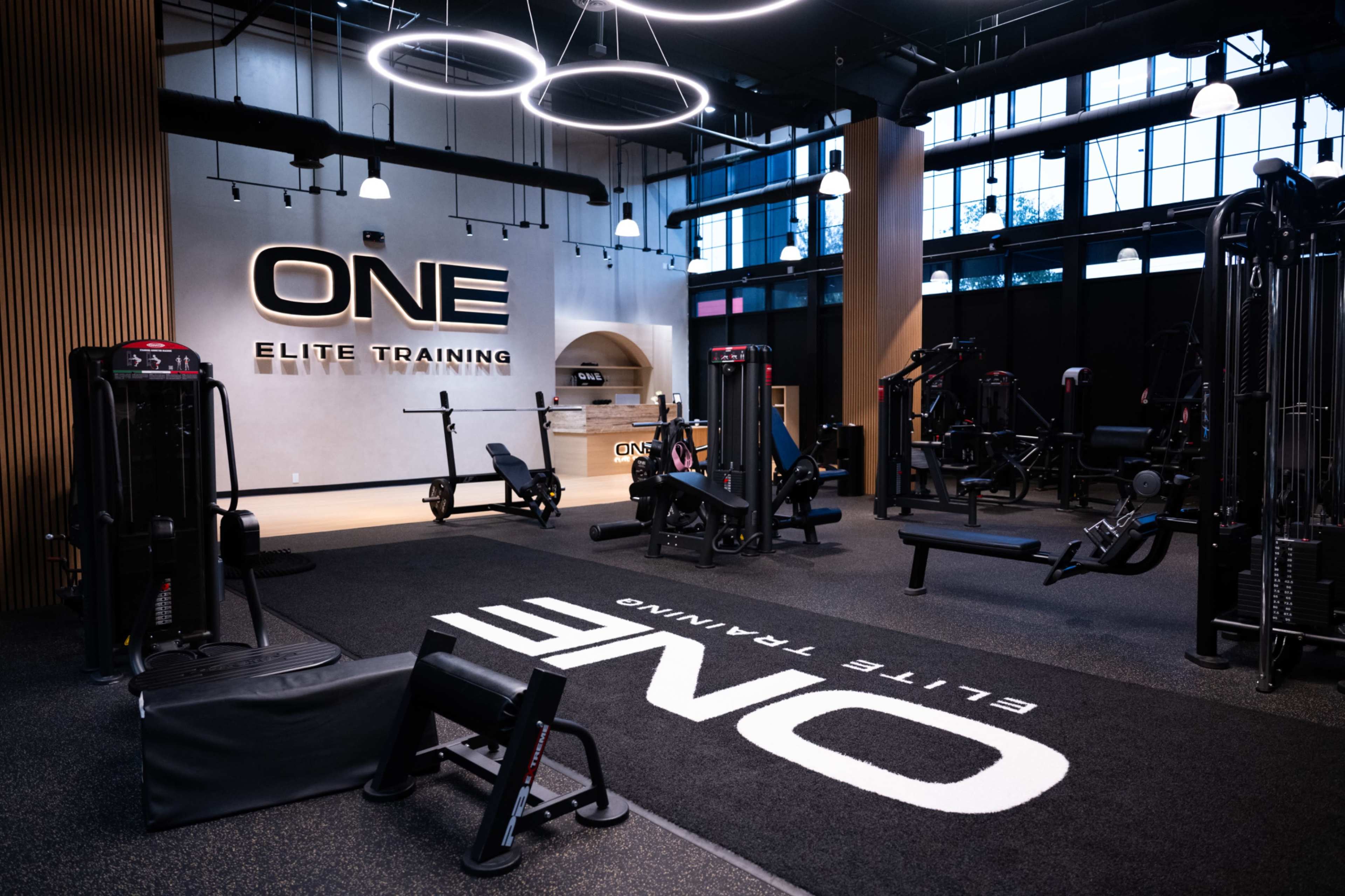The image shows a modern gym space with workout equipment neatly arranged and branding for "ONE Elite Training" on the wall.