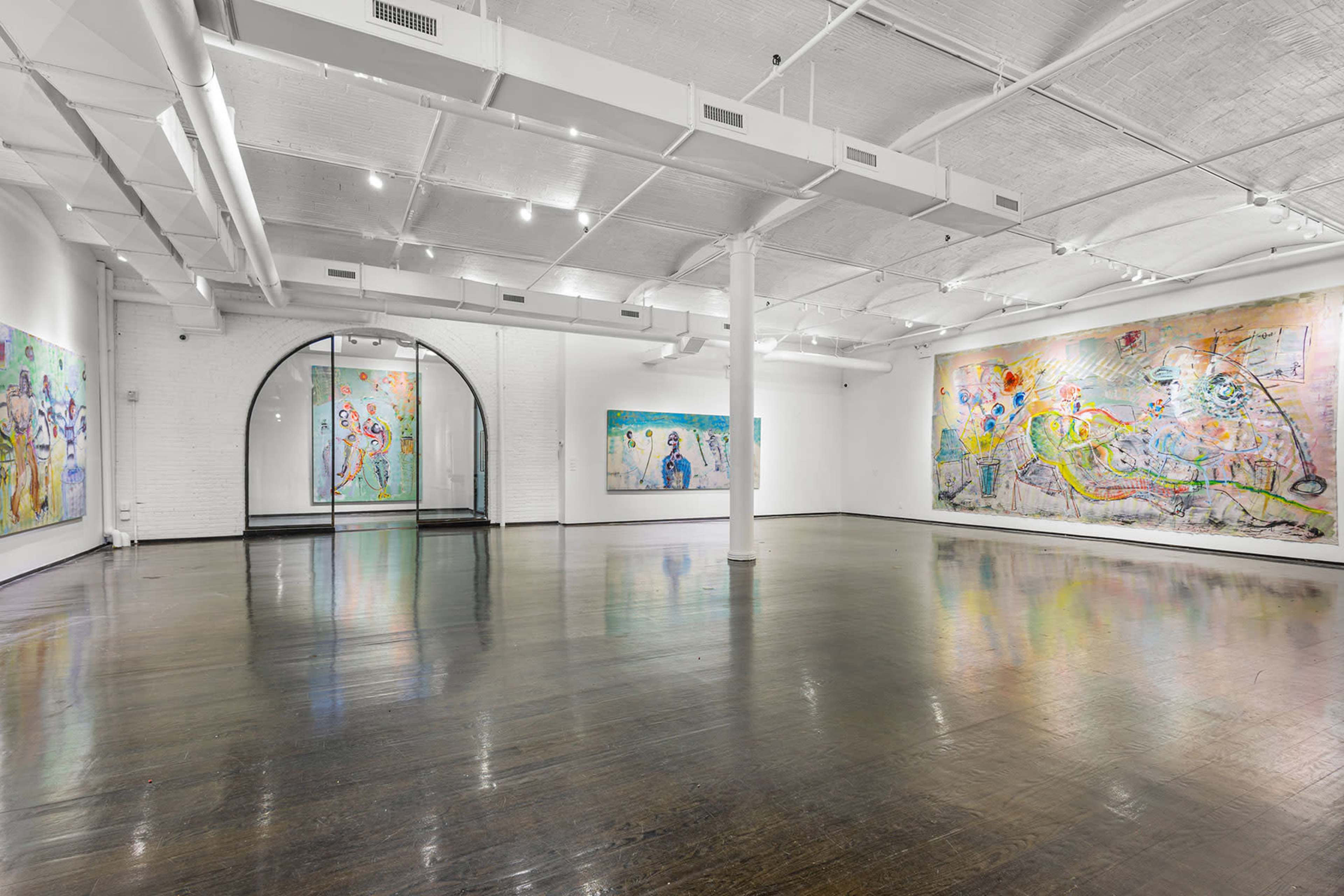 A spacious art gallery with white walls displaying large, colorful paintings, and polished wooden floors reflecting the light from overhead fixtures.