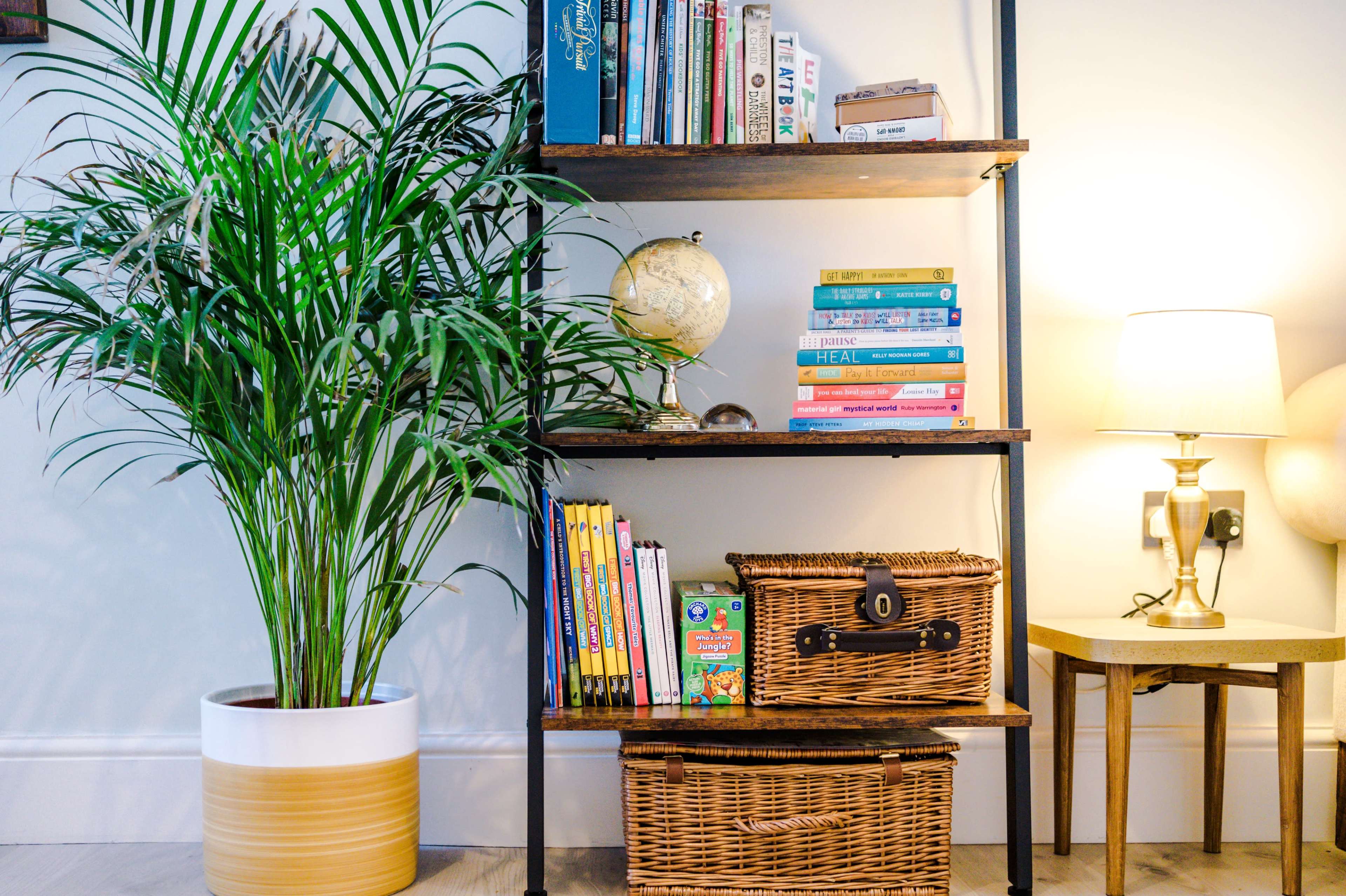 A bookshelf with various books, a globe, and a potted plant is positioned next to a lamp and a small table.