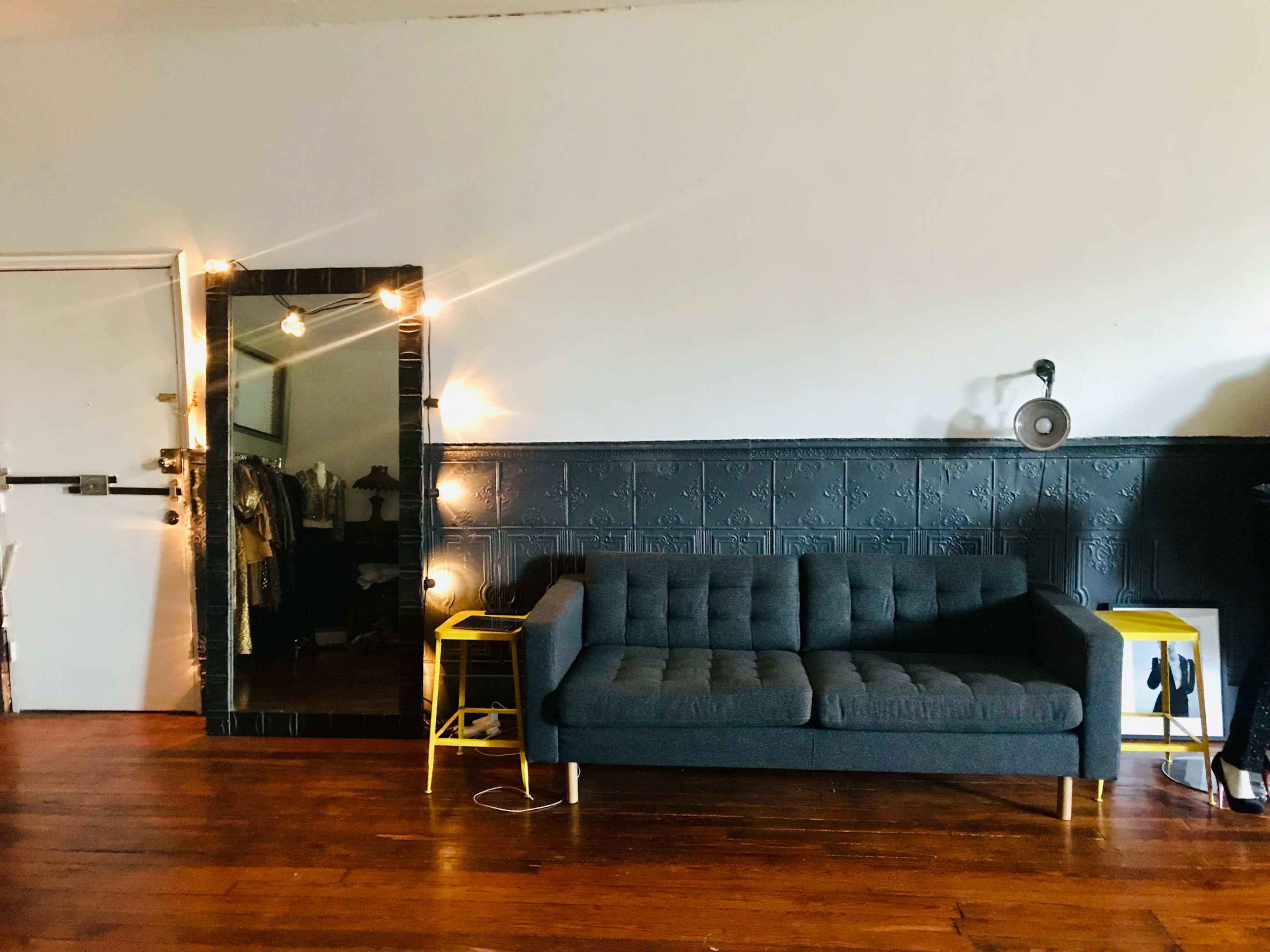 A gray sofa is positioned against a wall with a large mirror and string lights illuminating the room.