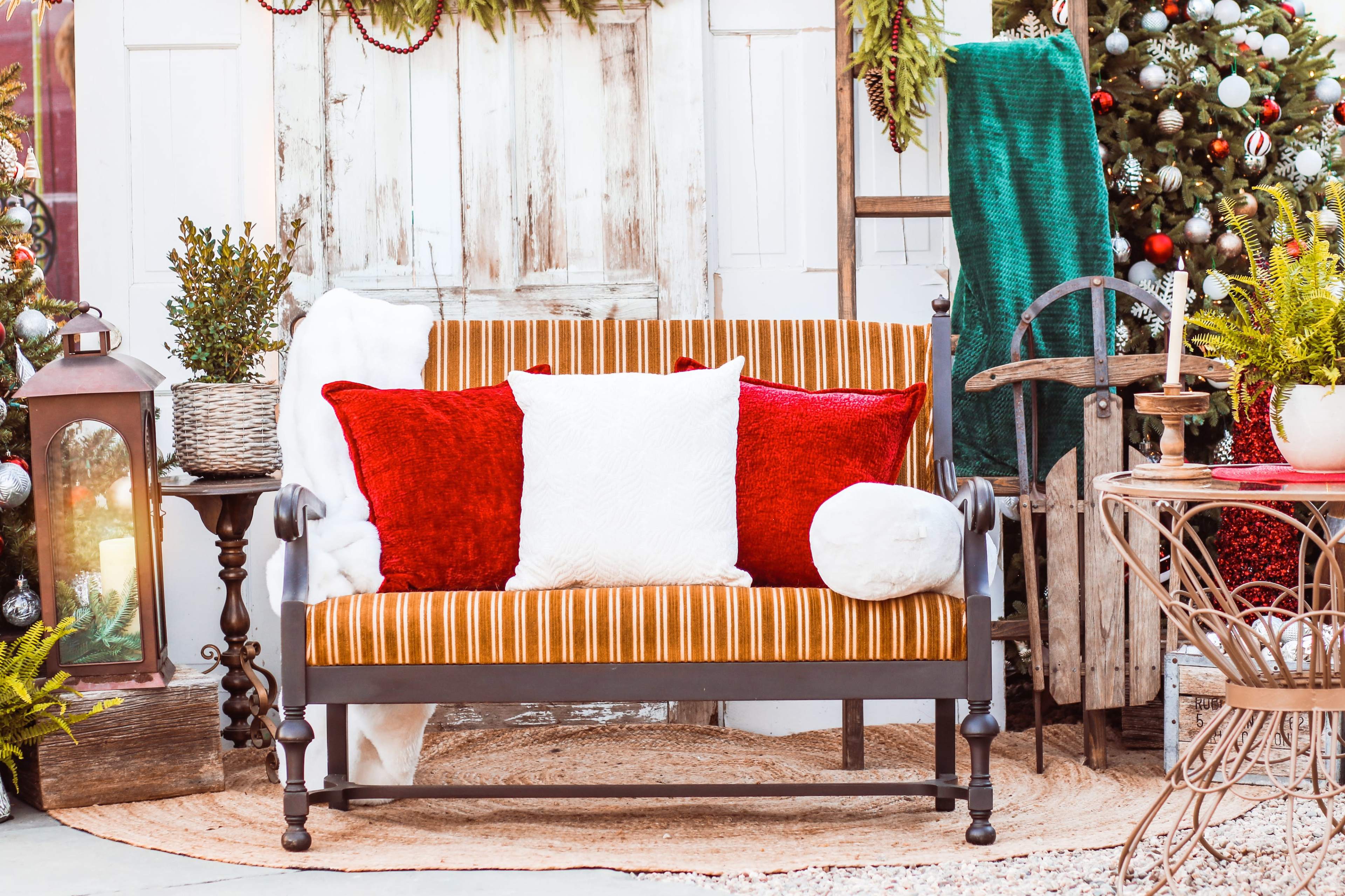 The image features a decorative outdoor seating area with a striped bench adorned with colorful cushions, surrounded by festive holiday decorations.