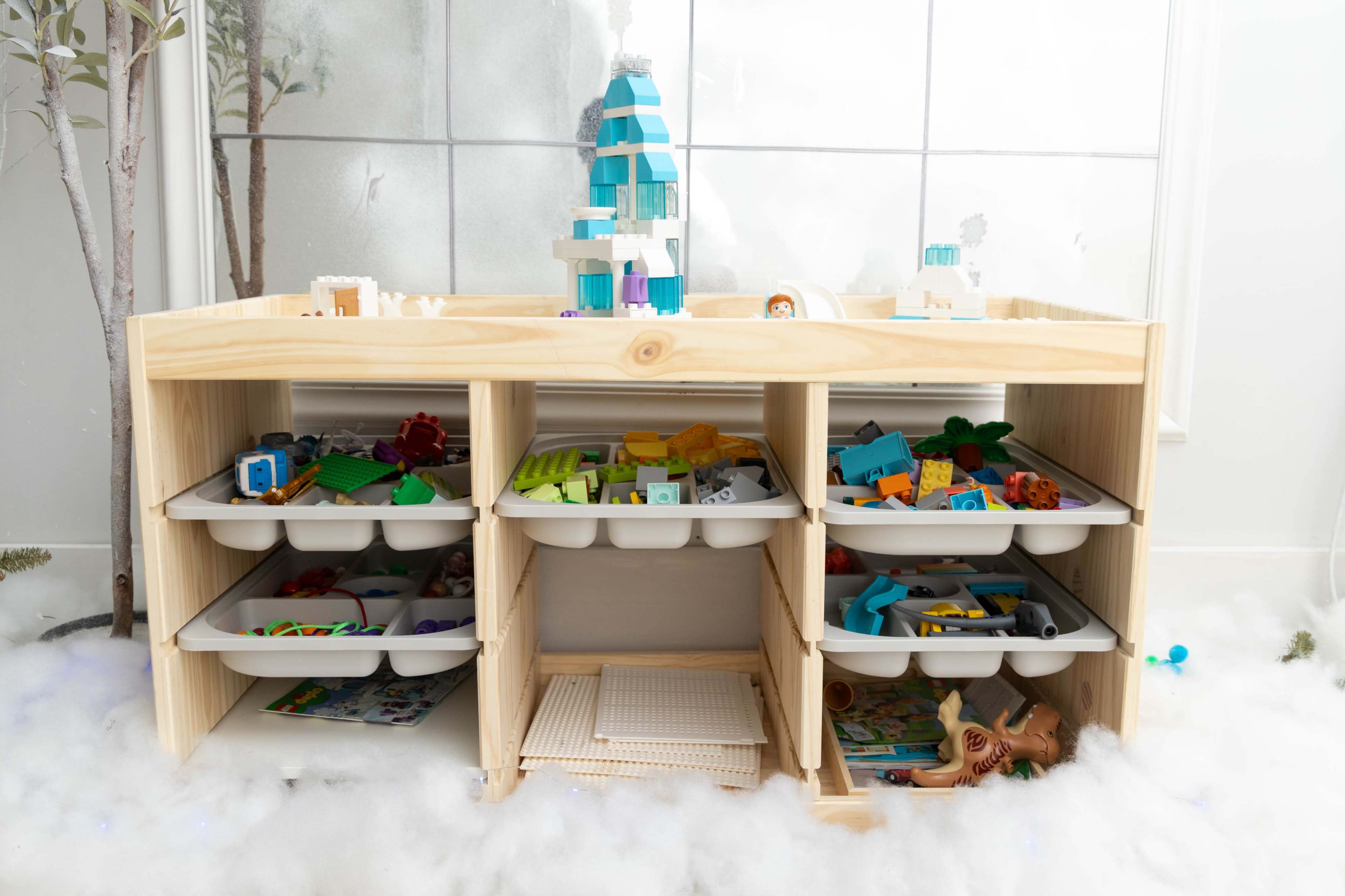 A wooden storage unit with multiple open shelves filled with colorful building blocks and toys, set against a snowy white backdrop.
