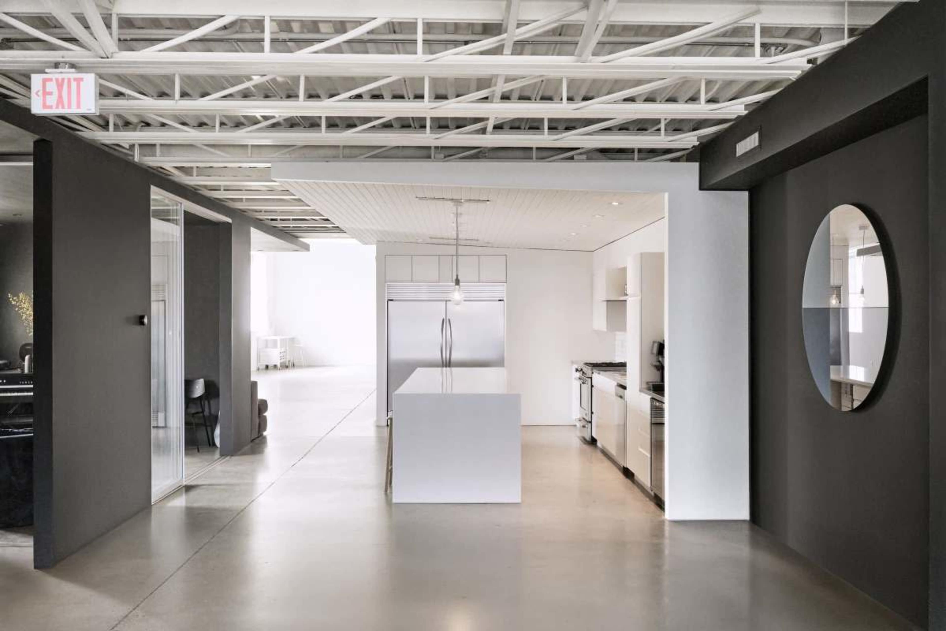 The image shows a modern kitchen with a large central island, stainless steel appliances, and a minimalist design, set in an open-concept space with exposed ceiling beams.
