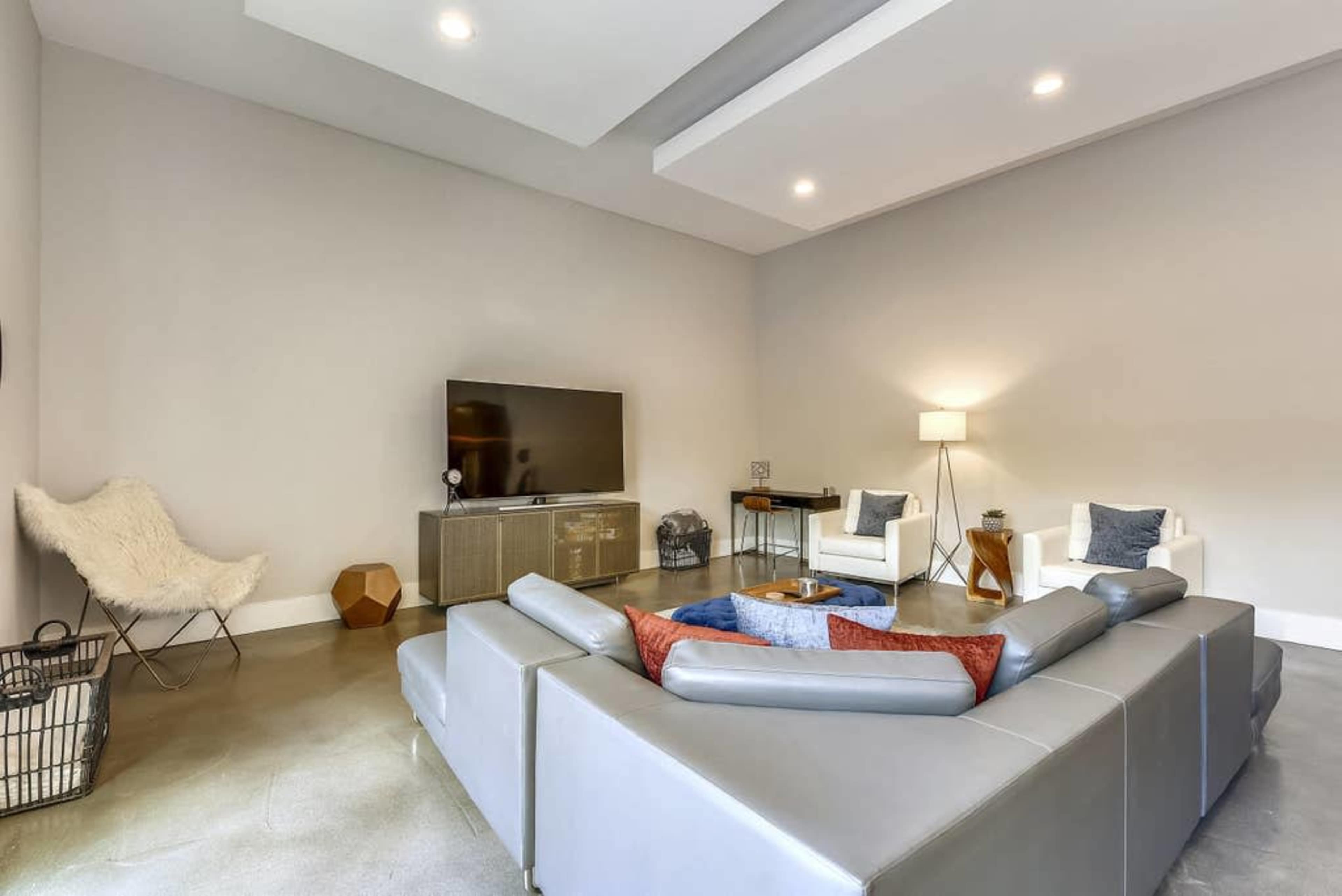 A modern living room features a gray sectional sofa, a large flat-screen TV on a media console, and two armchairs, all positioned around a low coffee table.