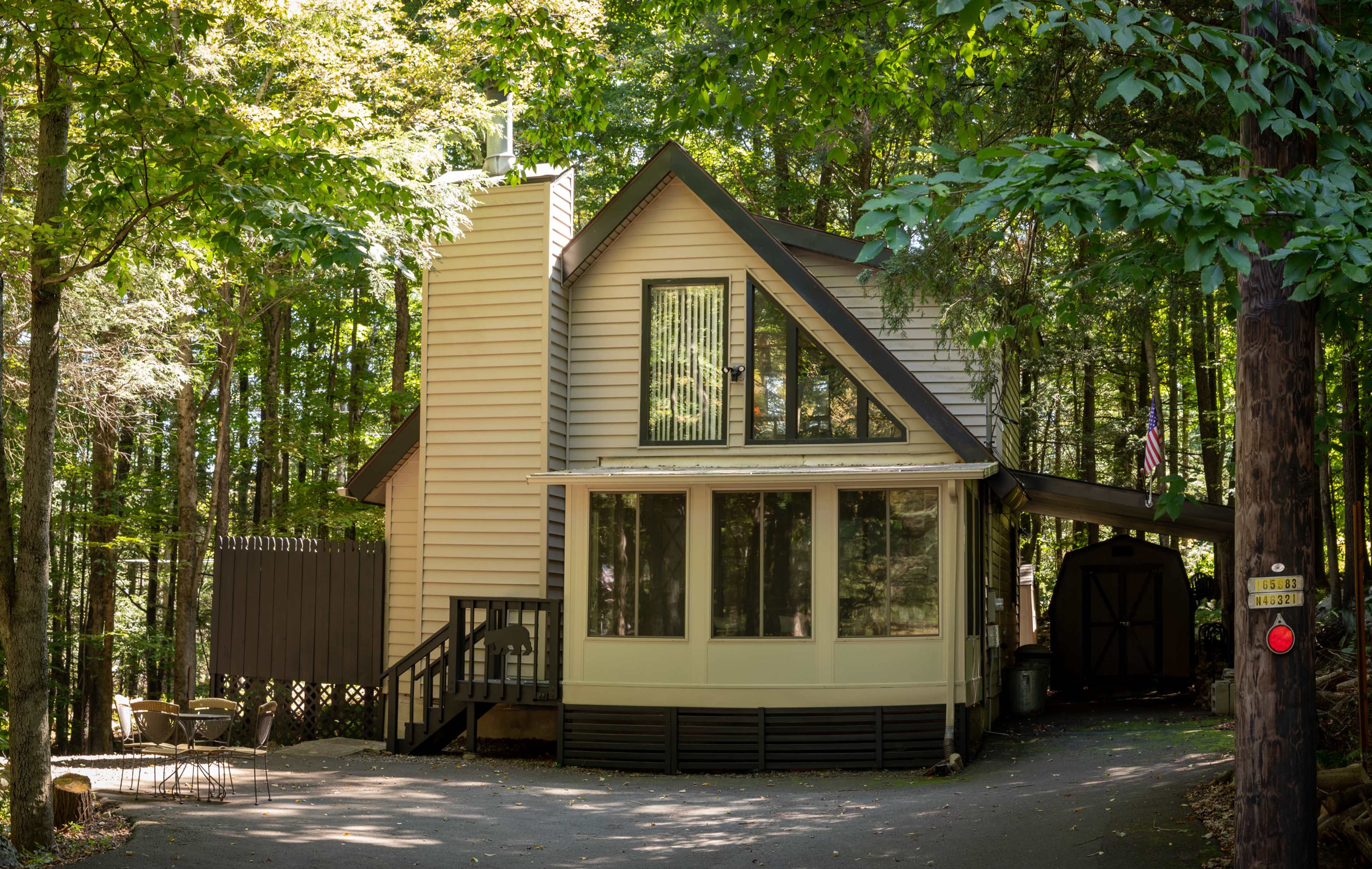 A modern two-story house with large windows sits among trees, featuring a sloped roof and a wooden deck.