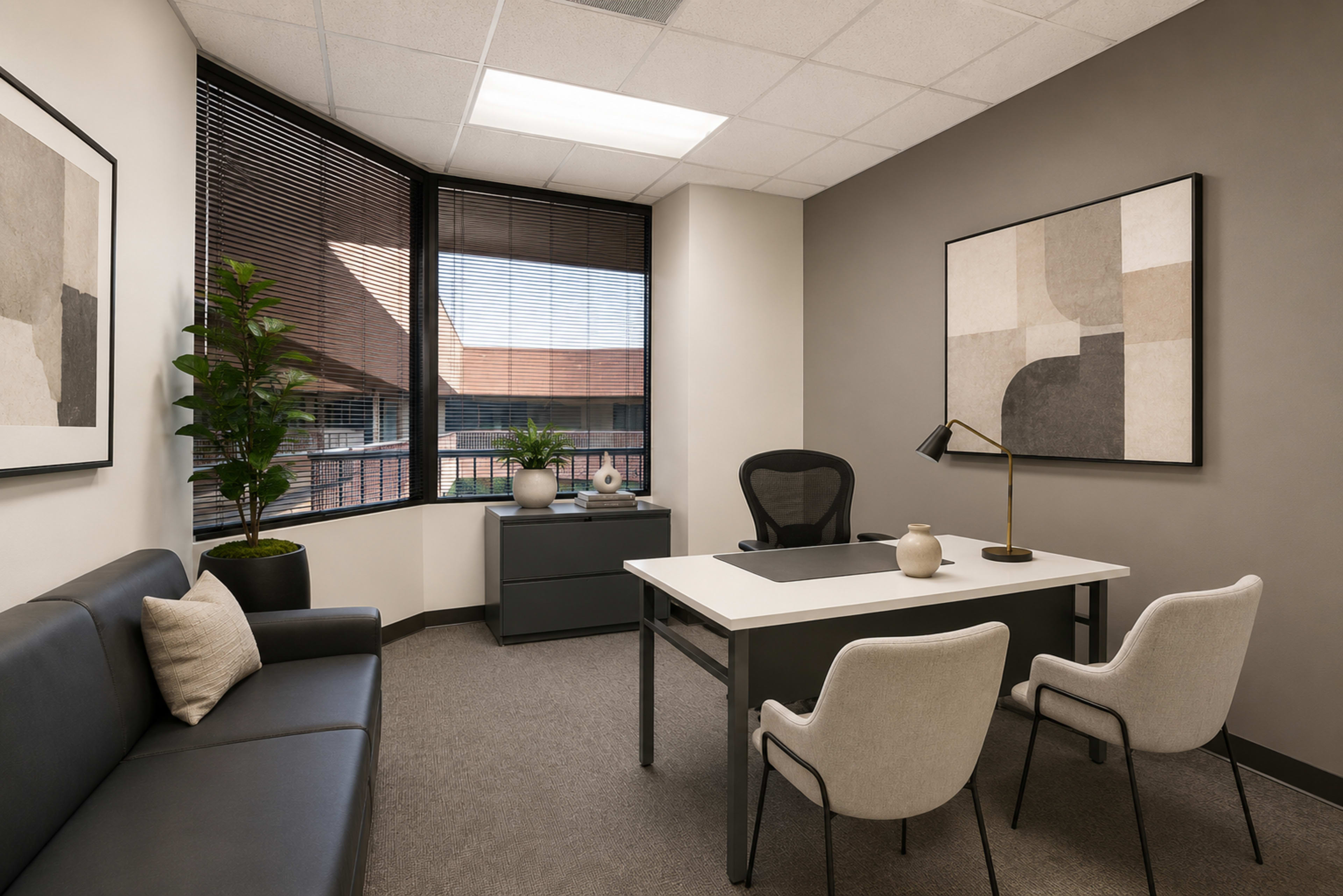 The image shows a modern office space featuring a desk, two chairs, a sofa, a plant, and a large abstract artwork on the wall.