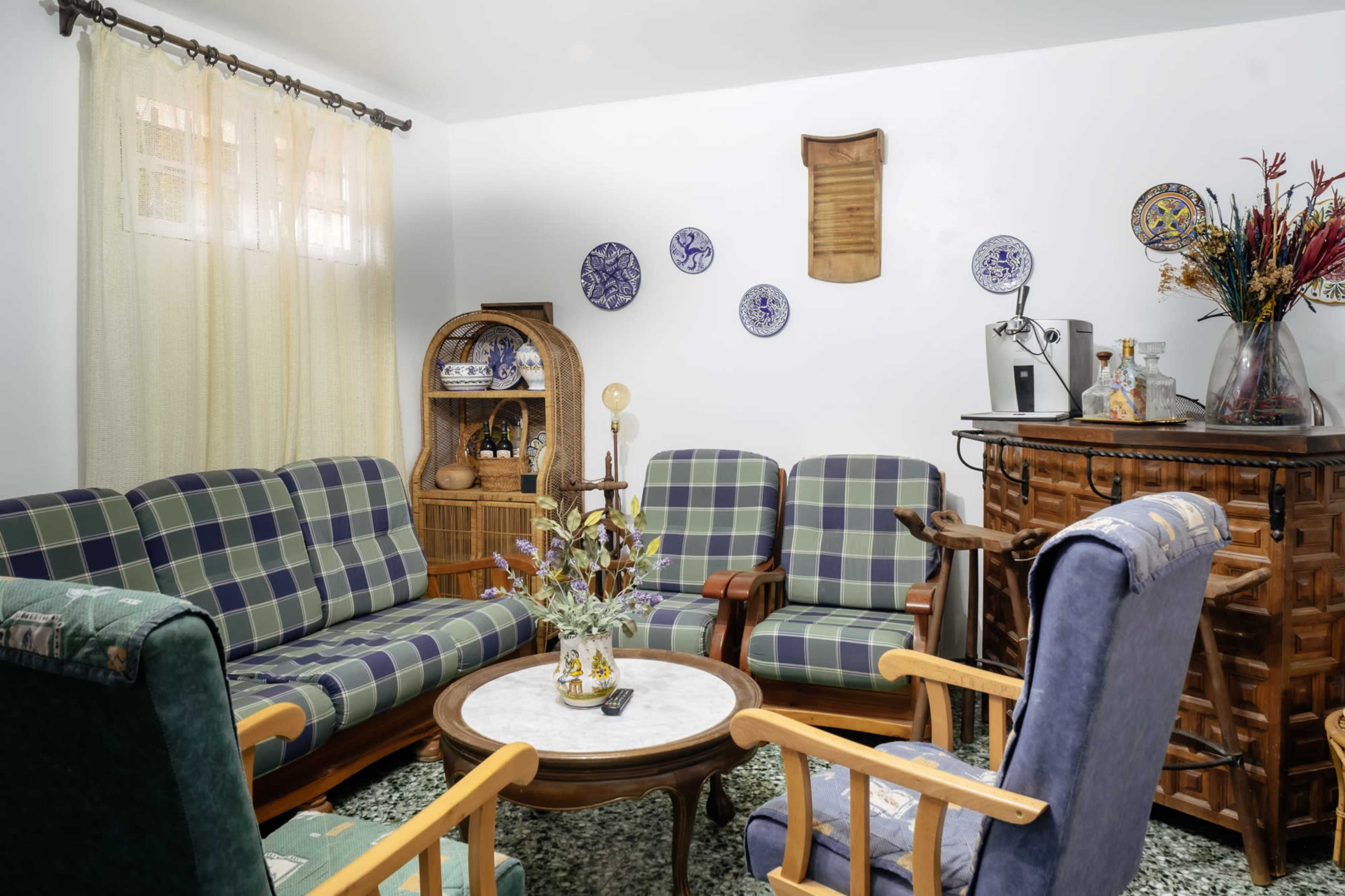 The living room features checkered sofas, a circular coffee table with a floral centerpiece, and a wooden bar with decorative plates on the walls.
