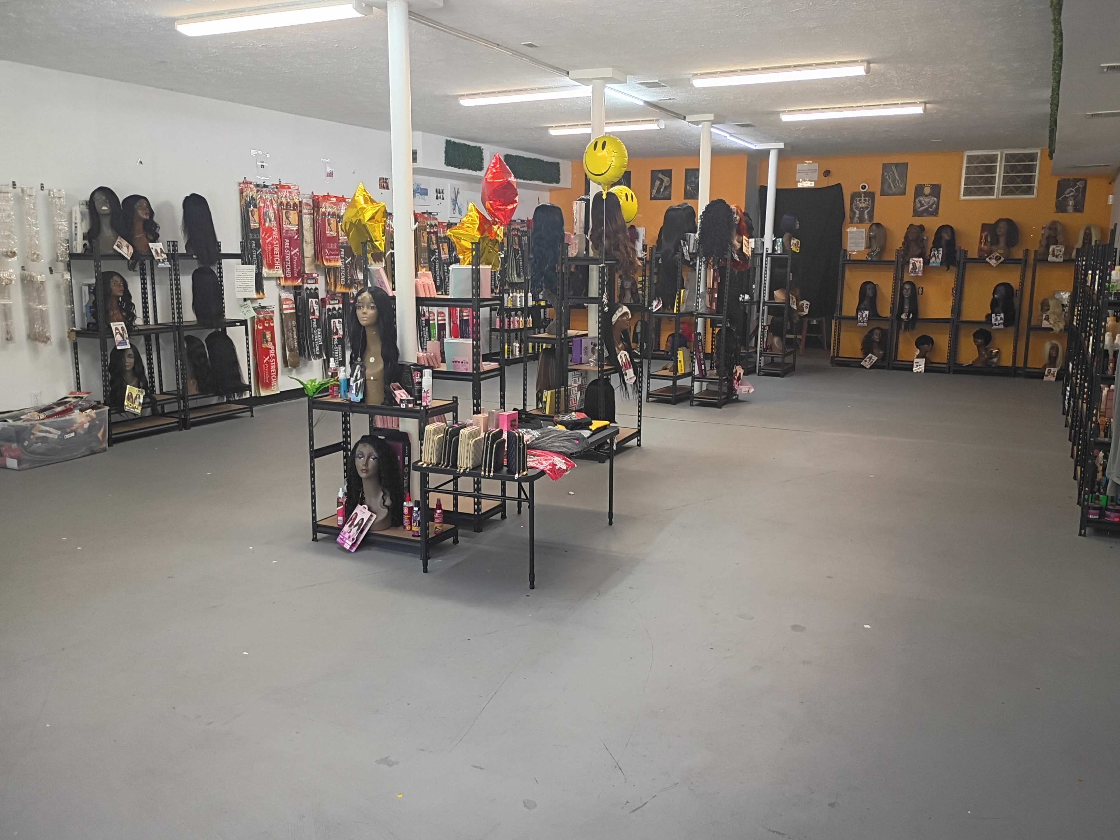 The image shows an interior of a store filled with shelves displaying various wigs and hair products, with an open floor space in the center.
