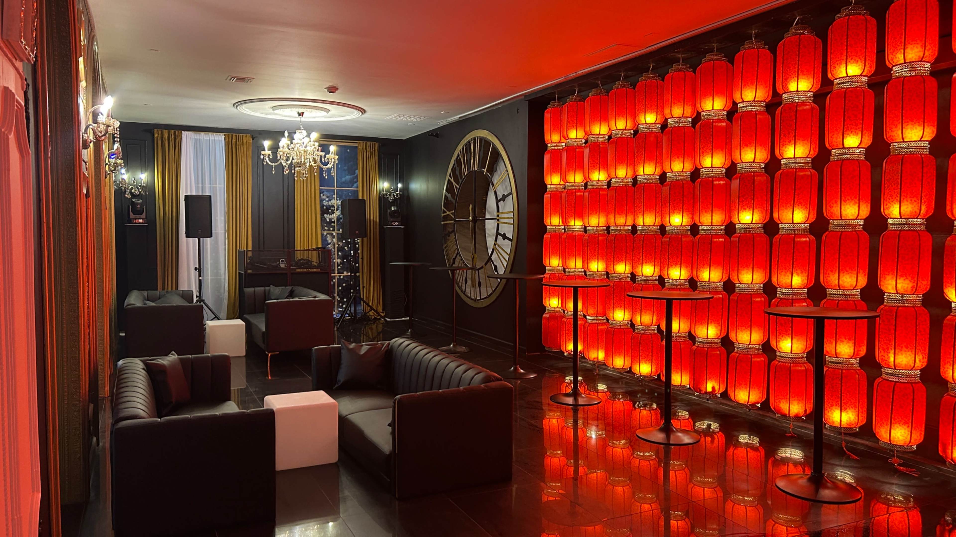 The scene features a stylish lounge area with black leather sofas, white tables, and a striking wall of illuminated red lanterns.