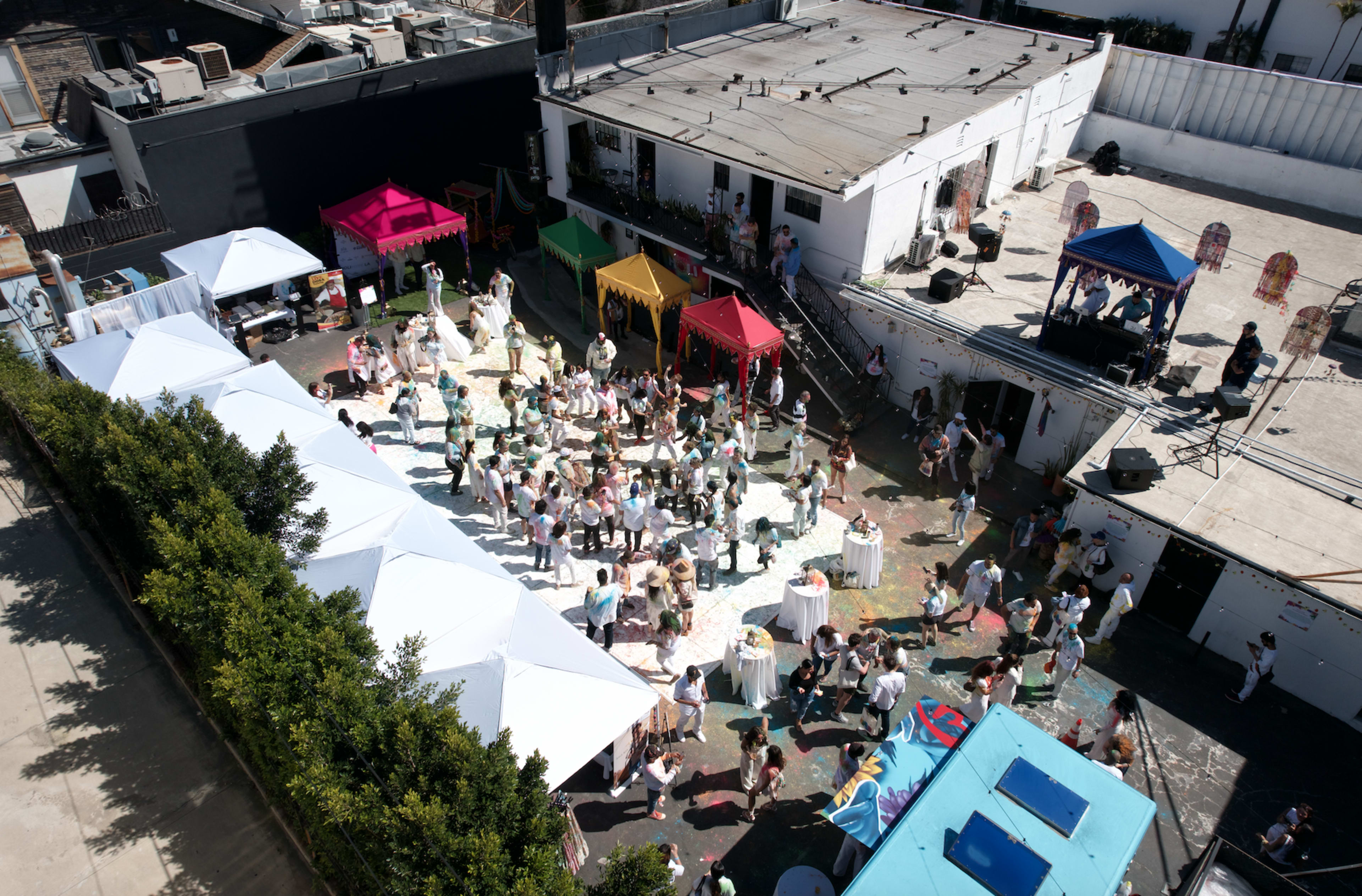 A large outdoor gathering is taking place in a courtyard filled with colorful tents, where people are dancing and socializing.