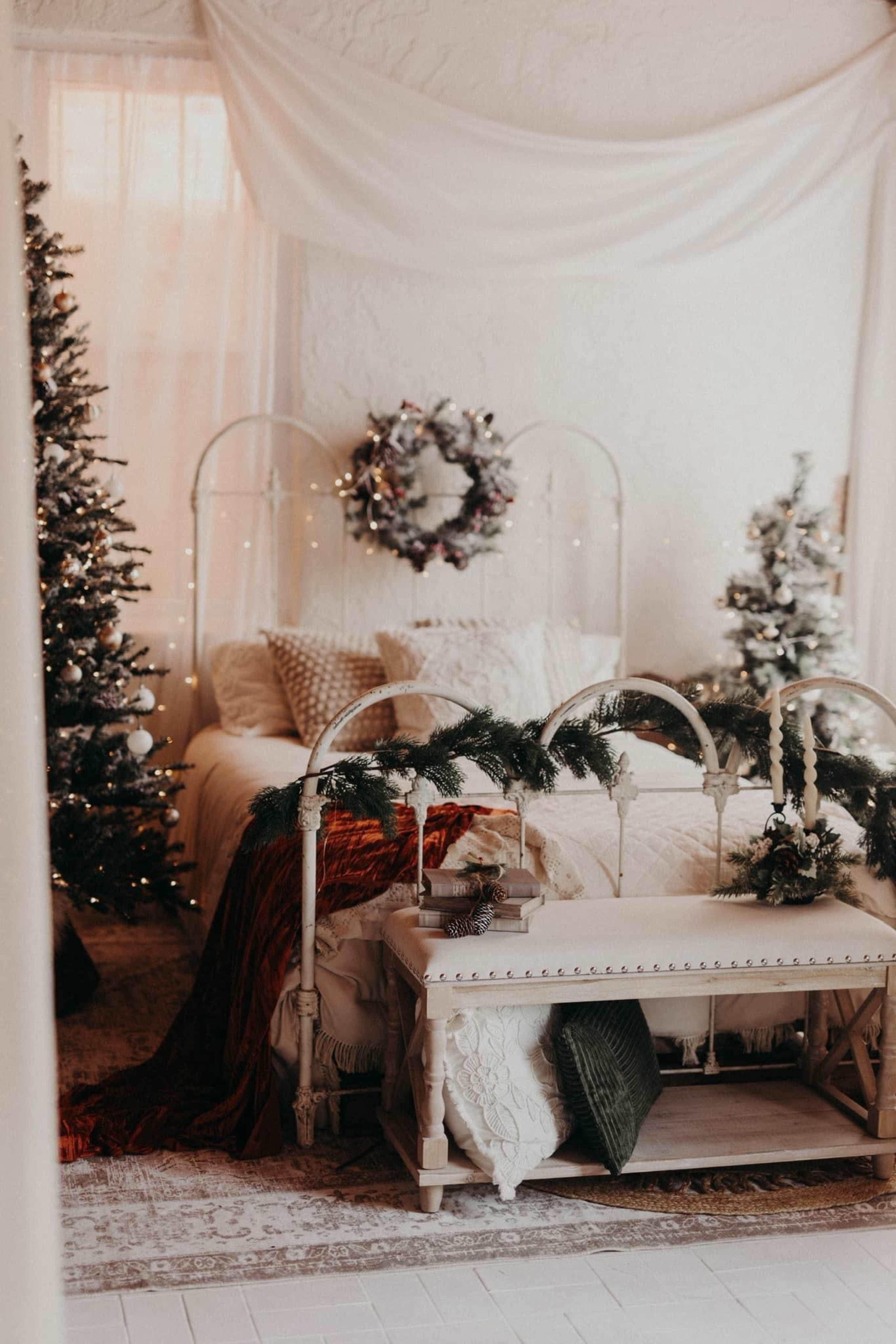 A cozy bedroom is adorned with Christmas trees, festive decorations, and a bed draped in warm blankets.