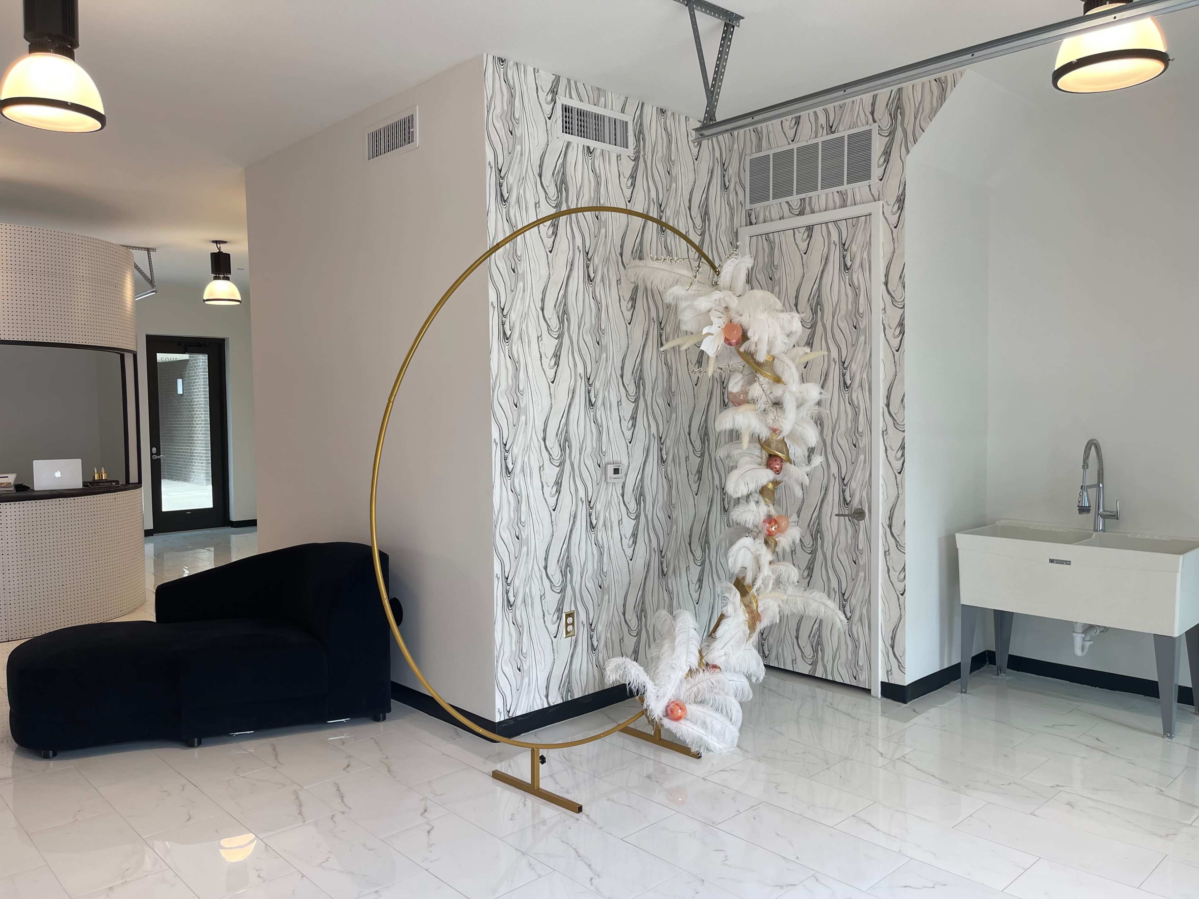 The image shows a modern interior space featuring a curved gold display stand with white decorative elements, a dark blue sofa, and a marble-tiled floor.