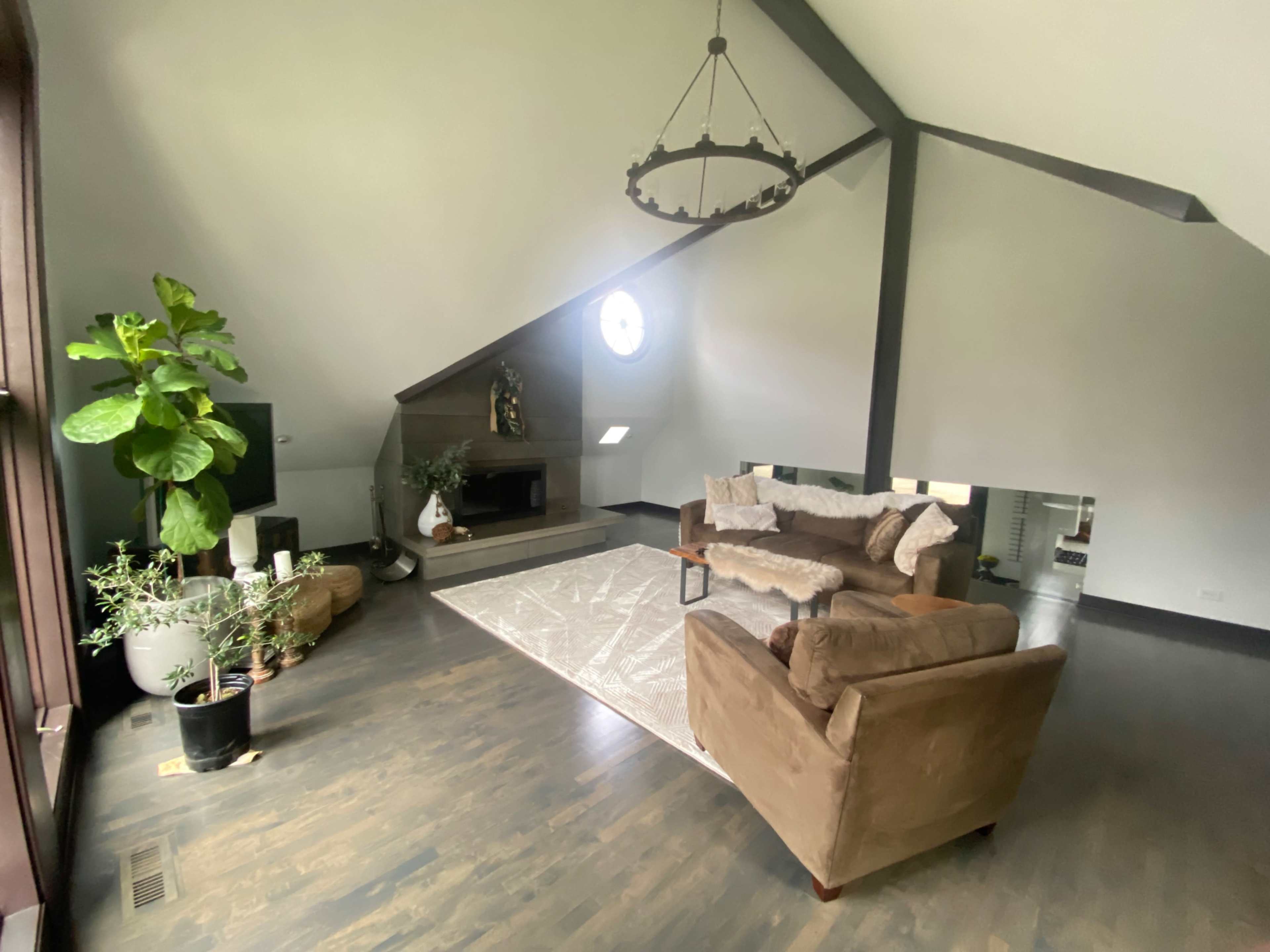 A spacious living room features a sloped ceiling, a fireplace, and seating arranged around a large area rug.