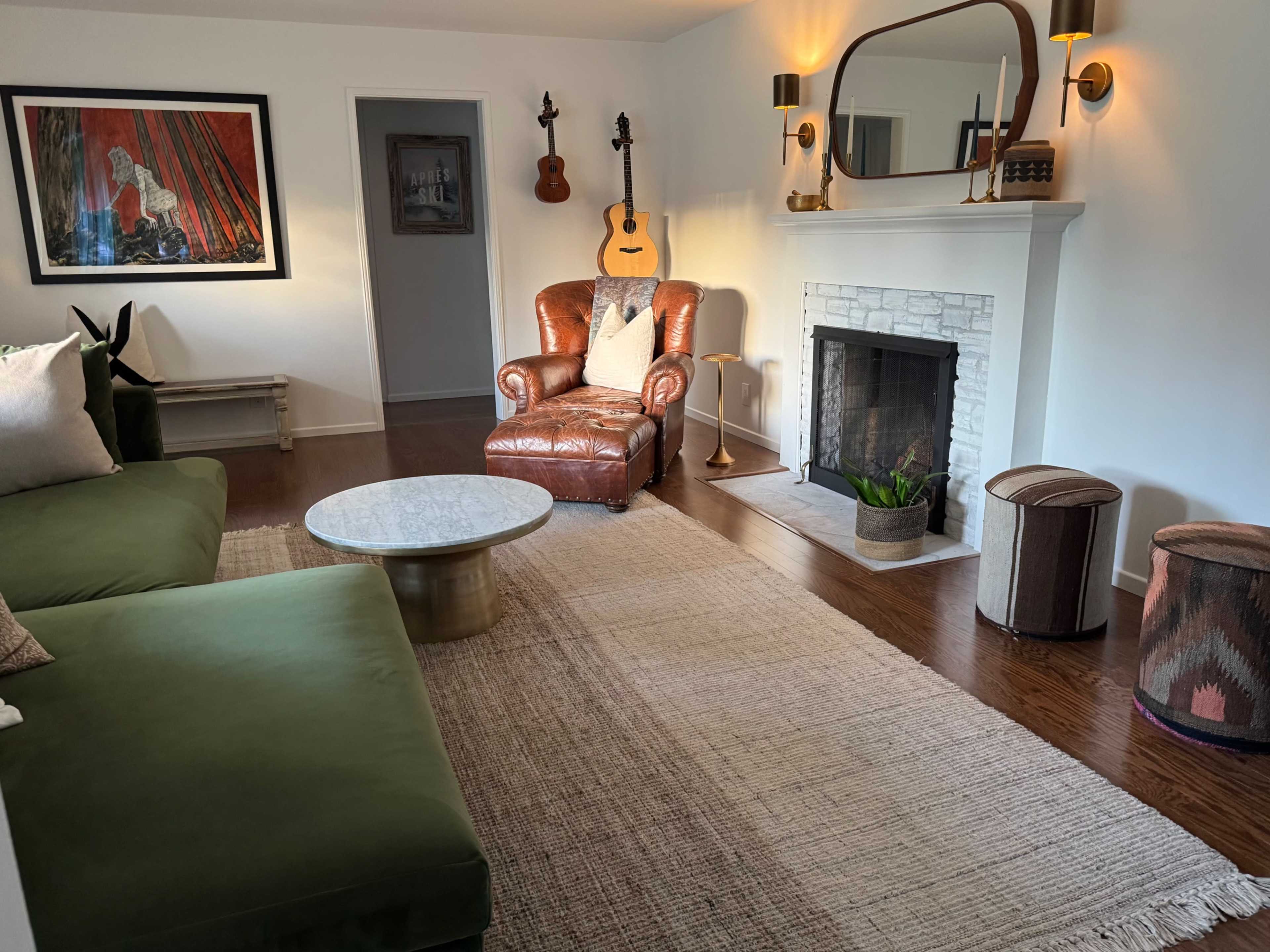 The living room features a green sectional sofa, a brown leather armchair, a coffee table, and a fireplace, with artwork and musical instruments adorning the walls.