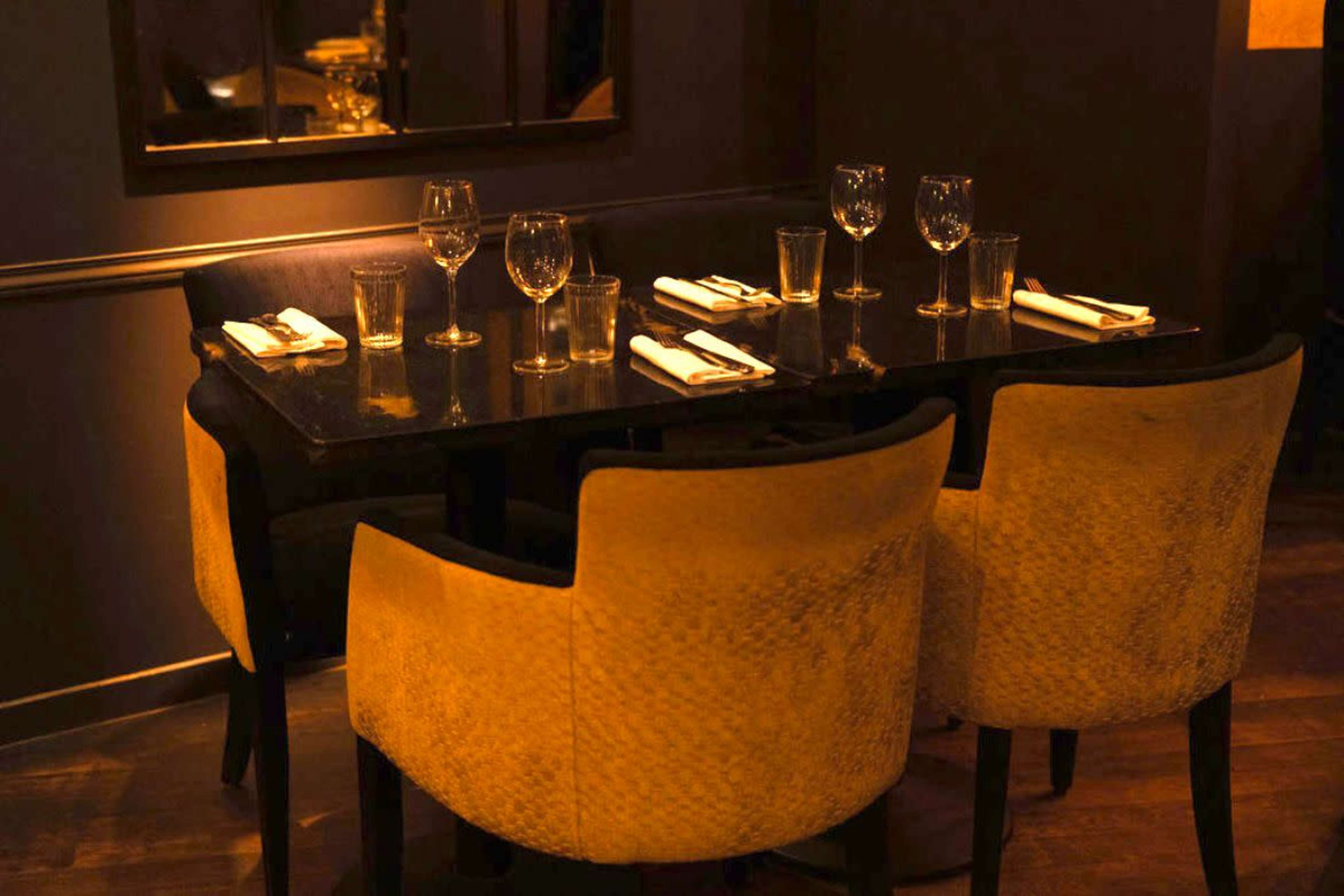 A dimly lit restaurant table is set with glassware and silverware, surrounded by plush yellow chairs.
