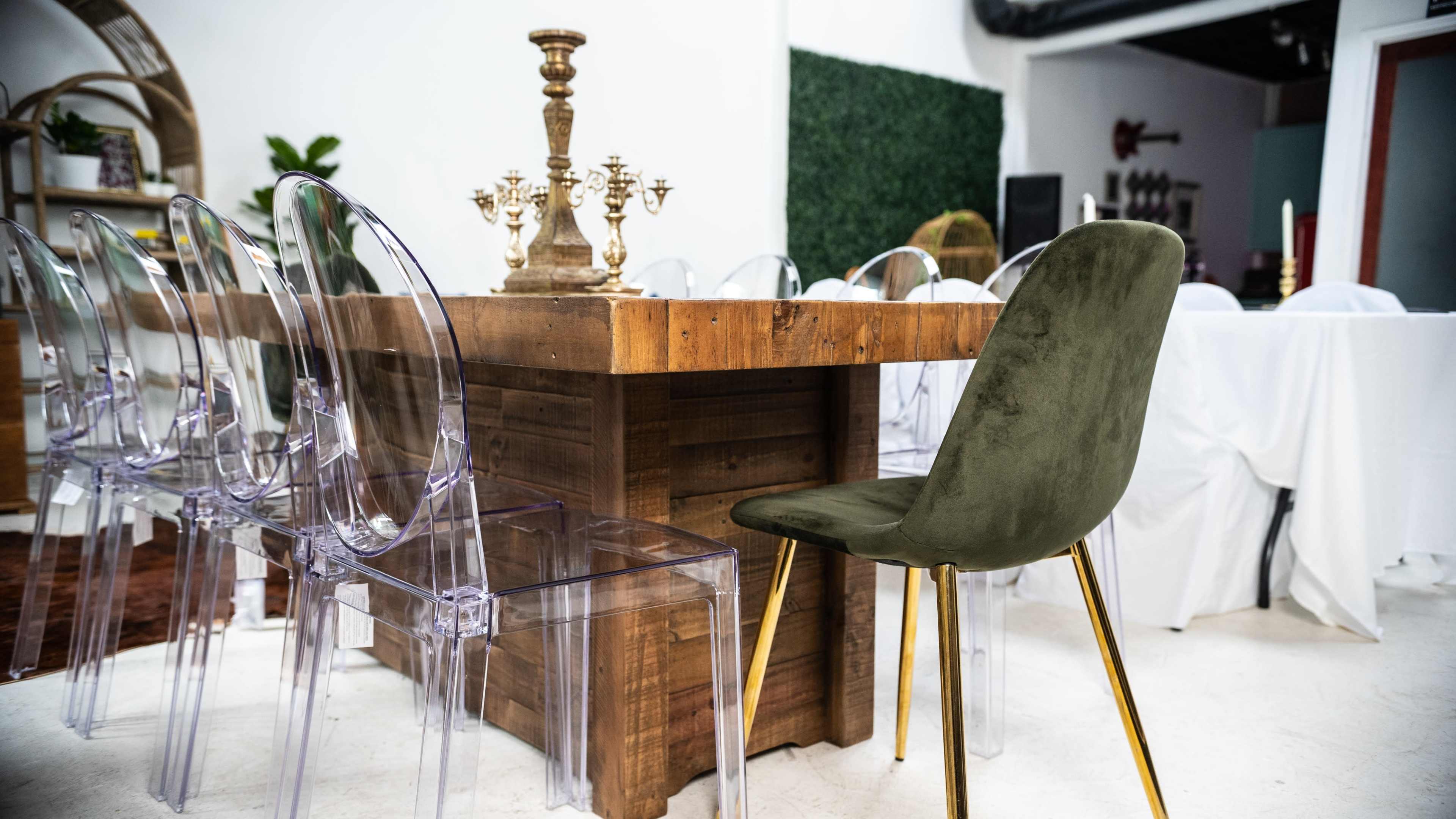 A wooden dining table is surrounded by clear acrylic chairs and a single green upholstered chair, with decorative candlesticks placed in the center.