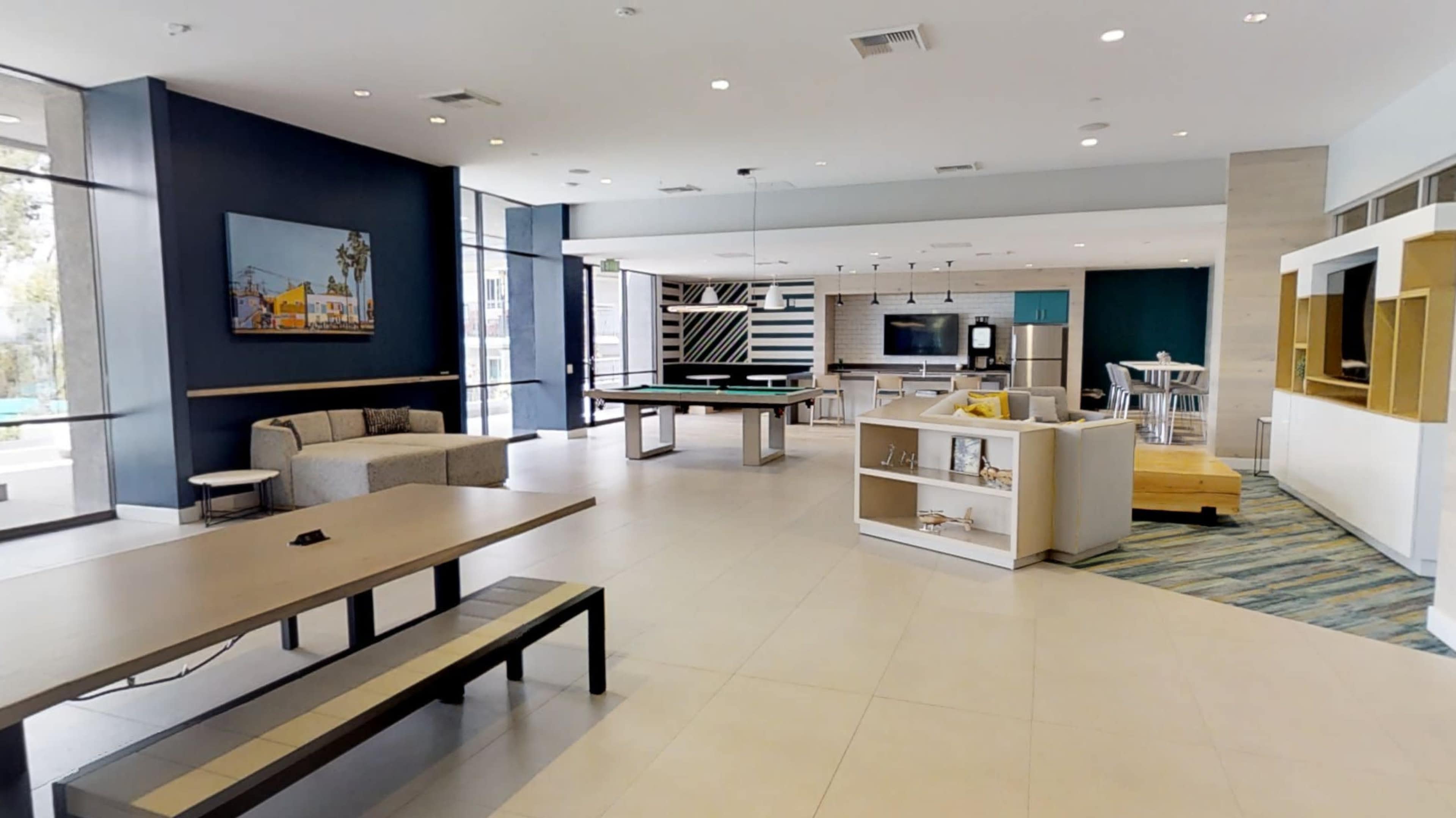 A modern common area with seating arrangements, a pool table, and a kitchenette in a well-lit interior space.