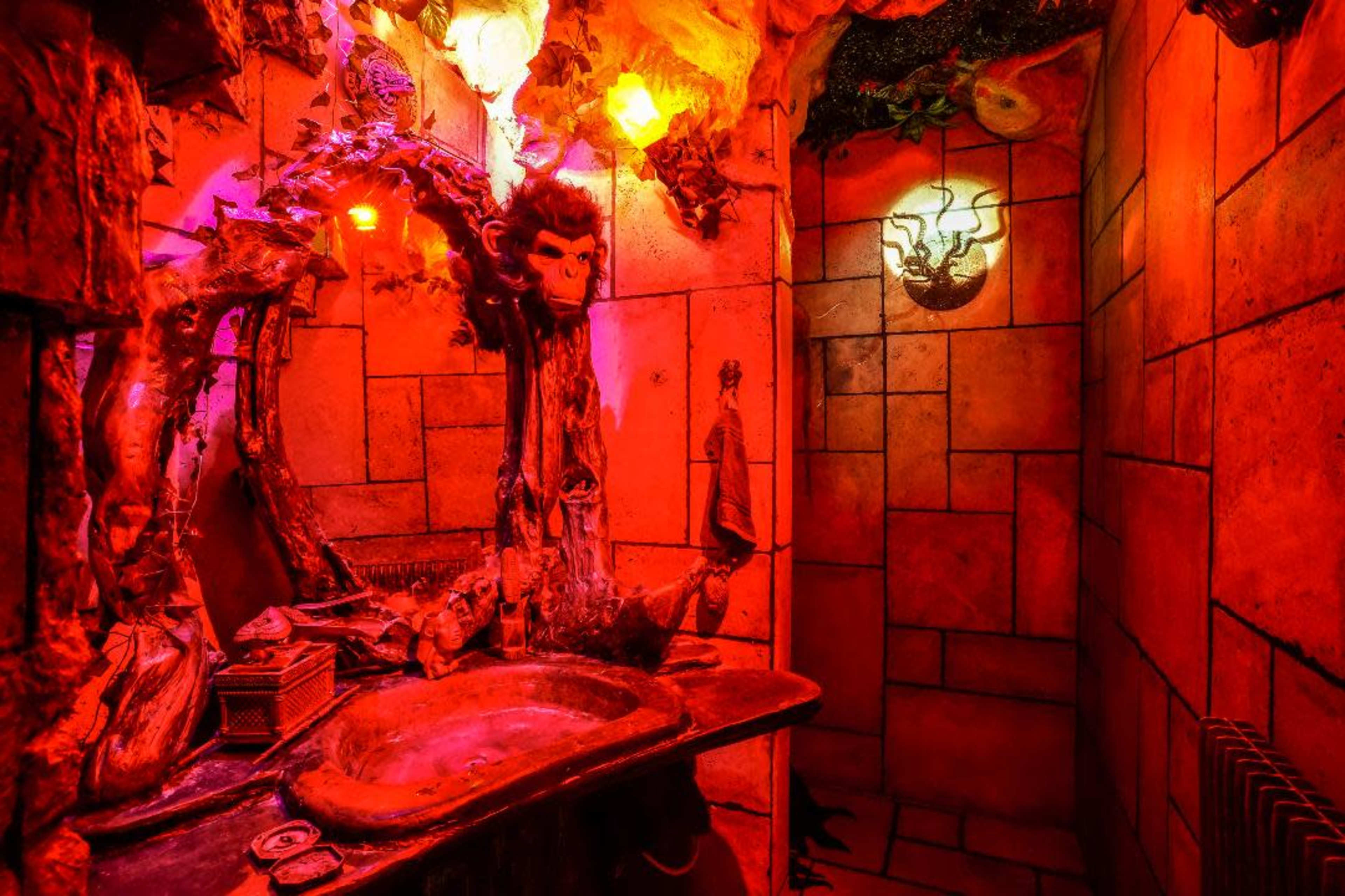 A bathroom with stone walls, a red hue from the lighting, and unique decorative elements, including a tree and animal carvings.
