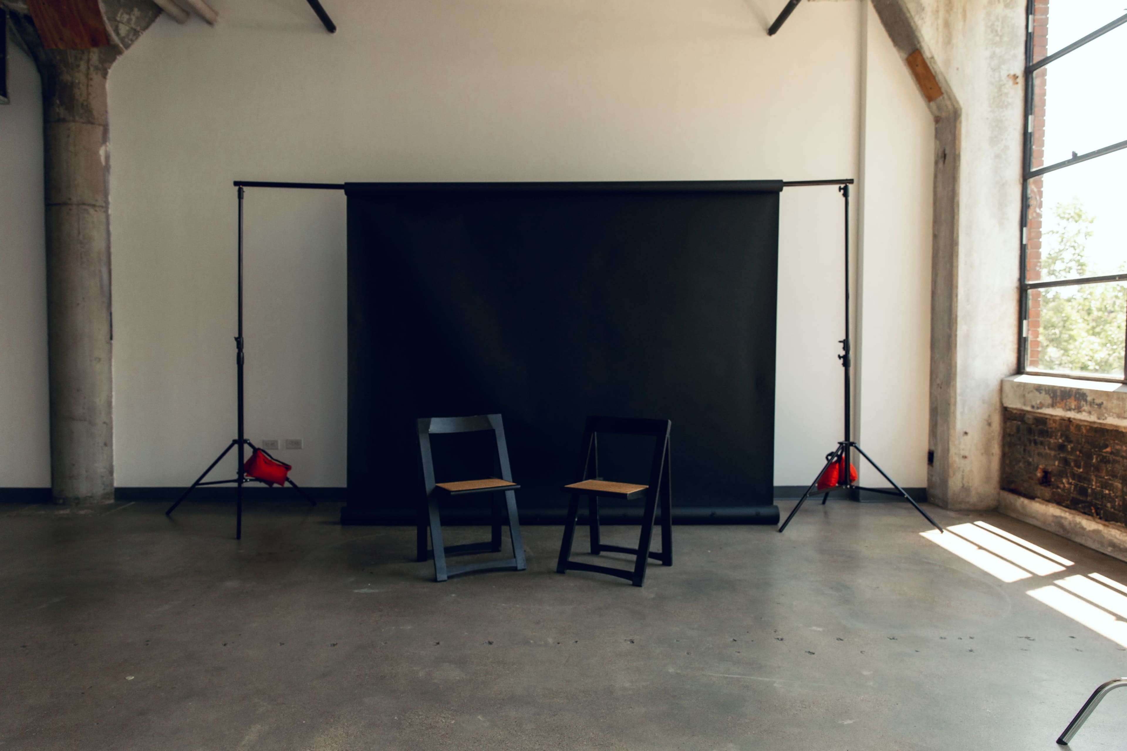 An empty studio space with two wooden chairs facing a black backdrop.