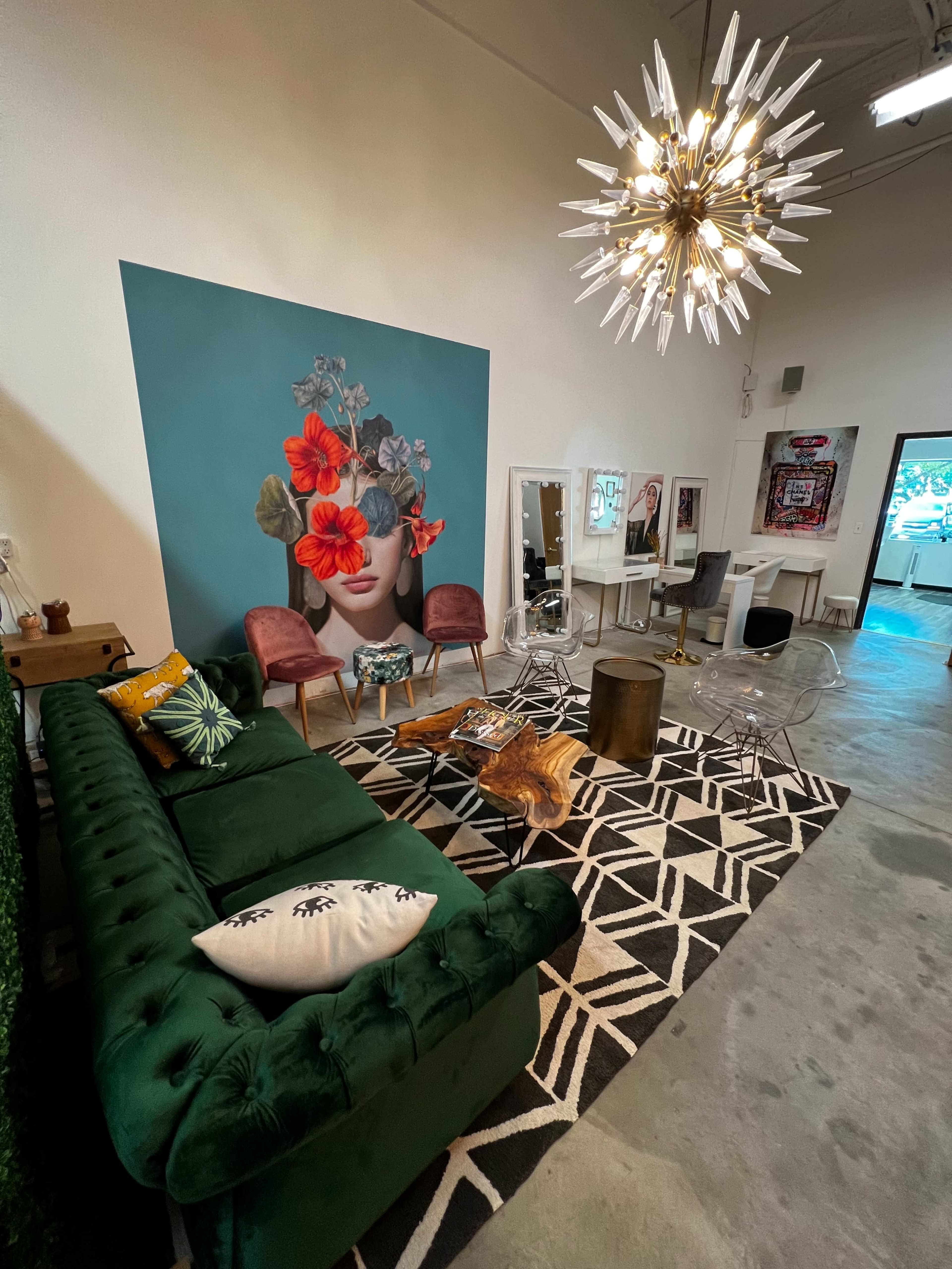 A modern living space featuring a green velvet sofa, a large floral mural, a stylish chandelier, and various seating arrangements on a geometric patterned rug.