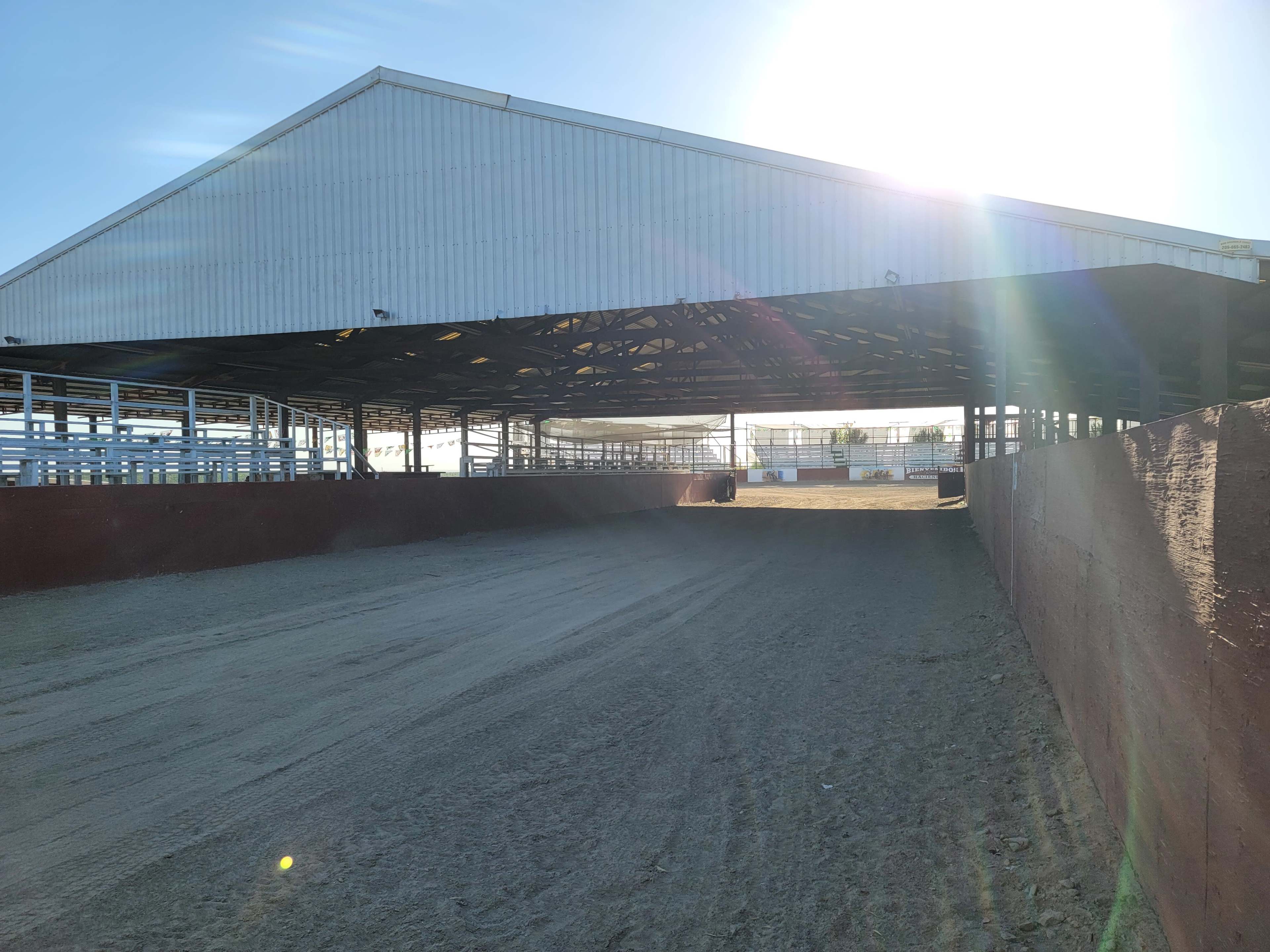A covered arena with a sandy floor and a bright light coming from the sun in the background.