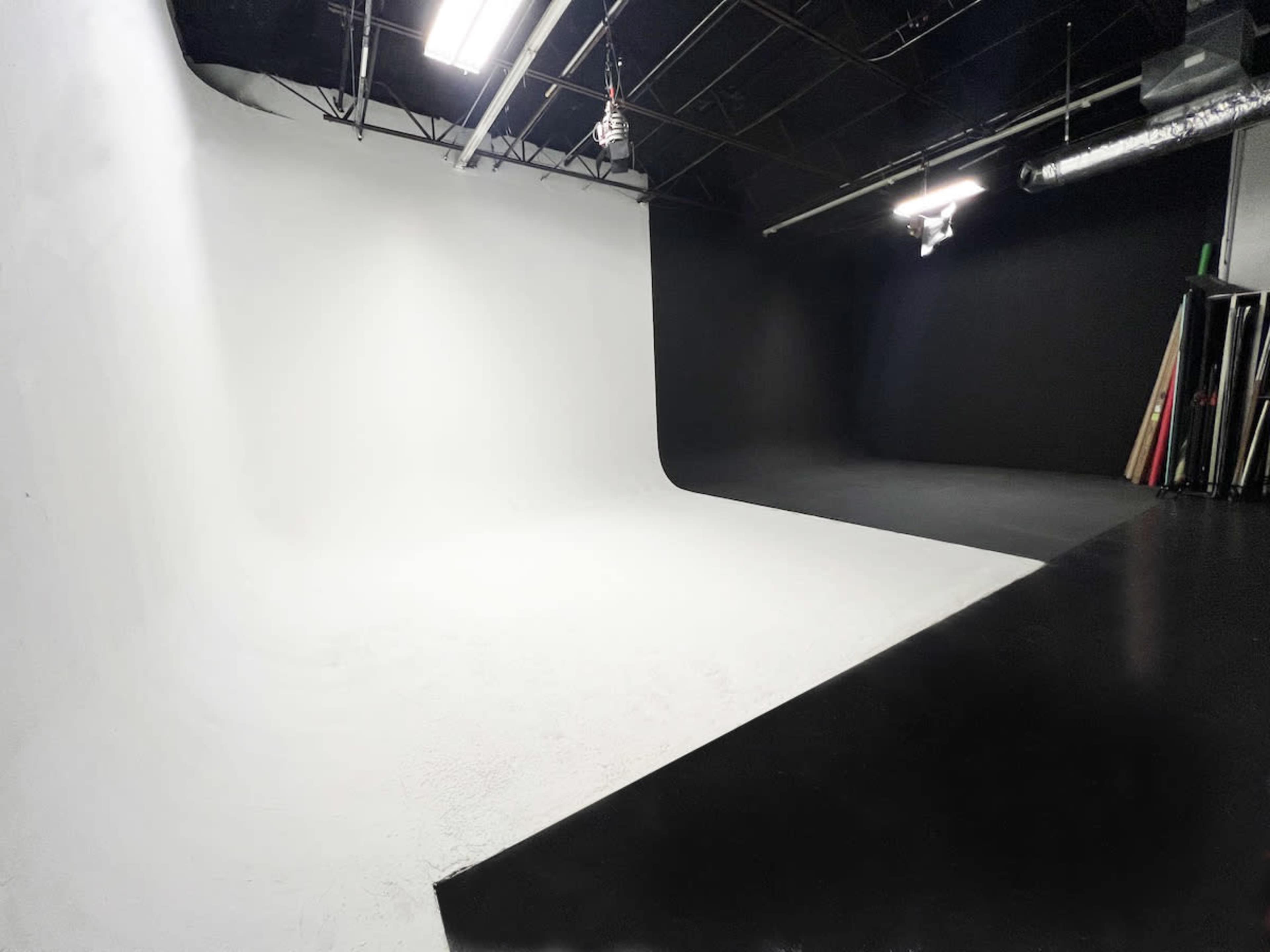 The image shows a spacious photography studio featuring a seamless white backdrop and a black side wall.