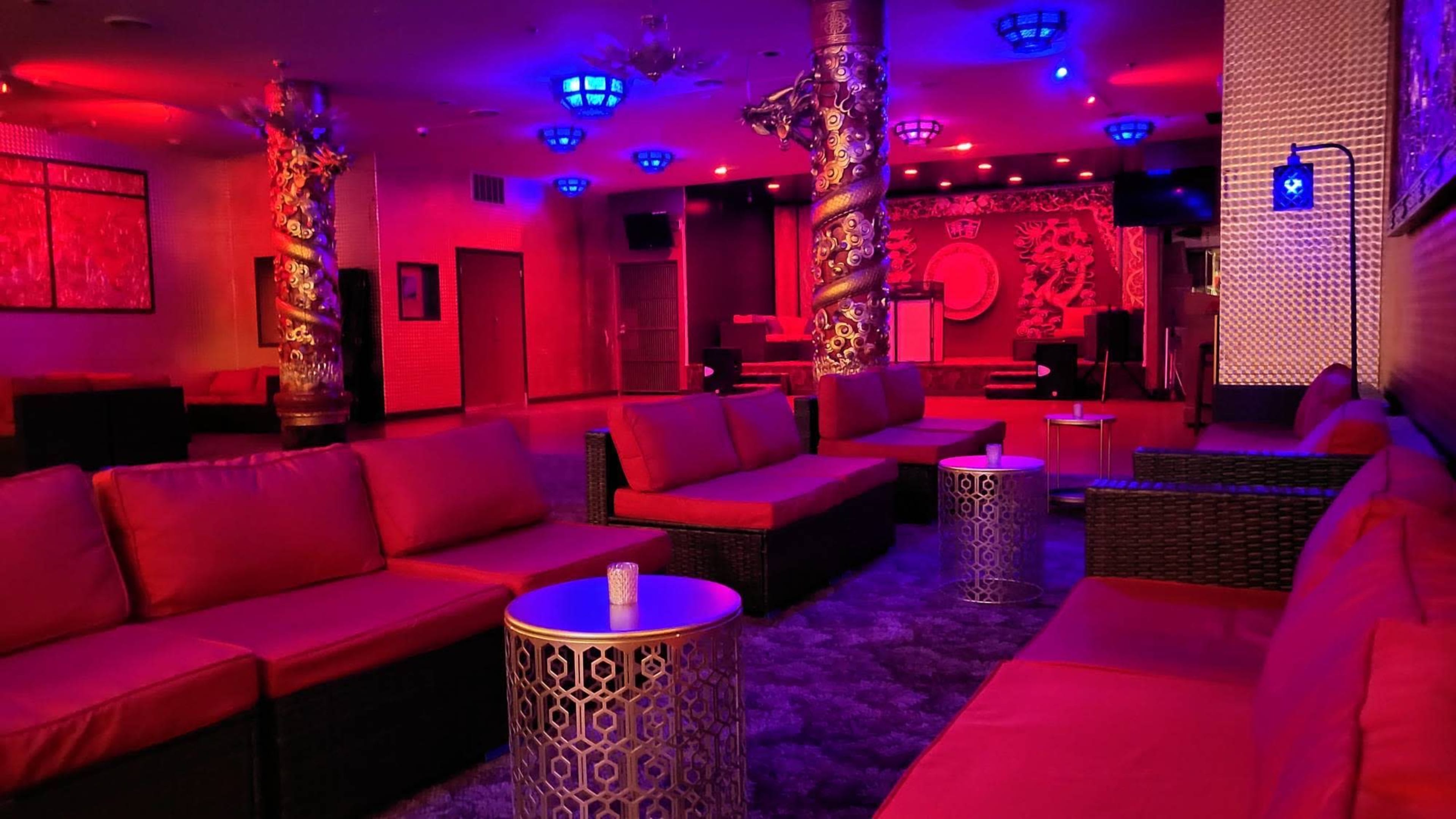 The image shows an interior lounge space with red lighting, featuring several red couches and metallic tables.