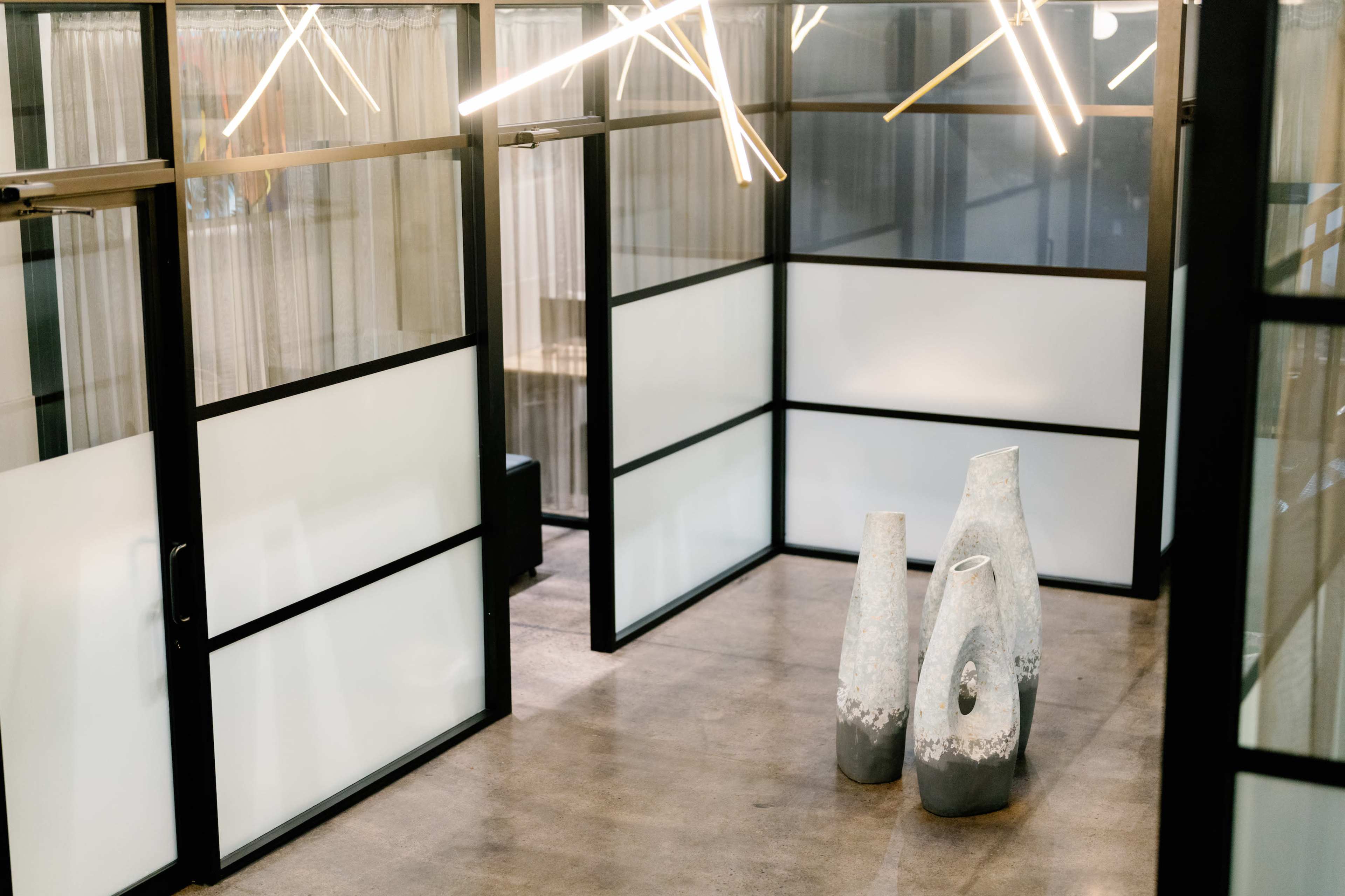 The image shows a modern interior space with frosted glass partitions and three large, abstract vases positioned on a polished concrete floor.