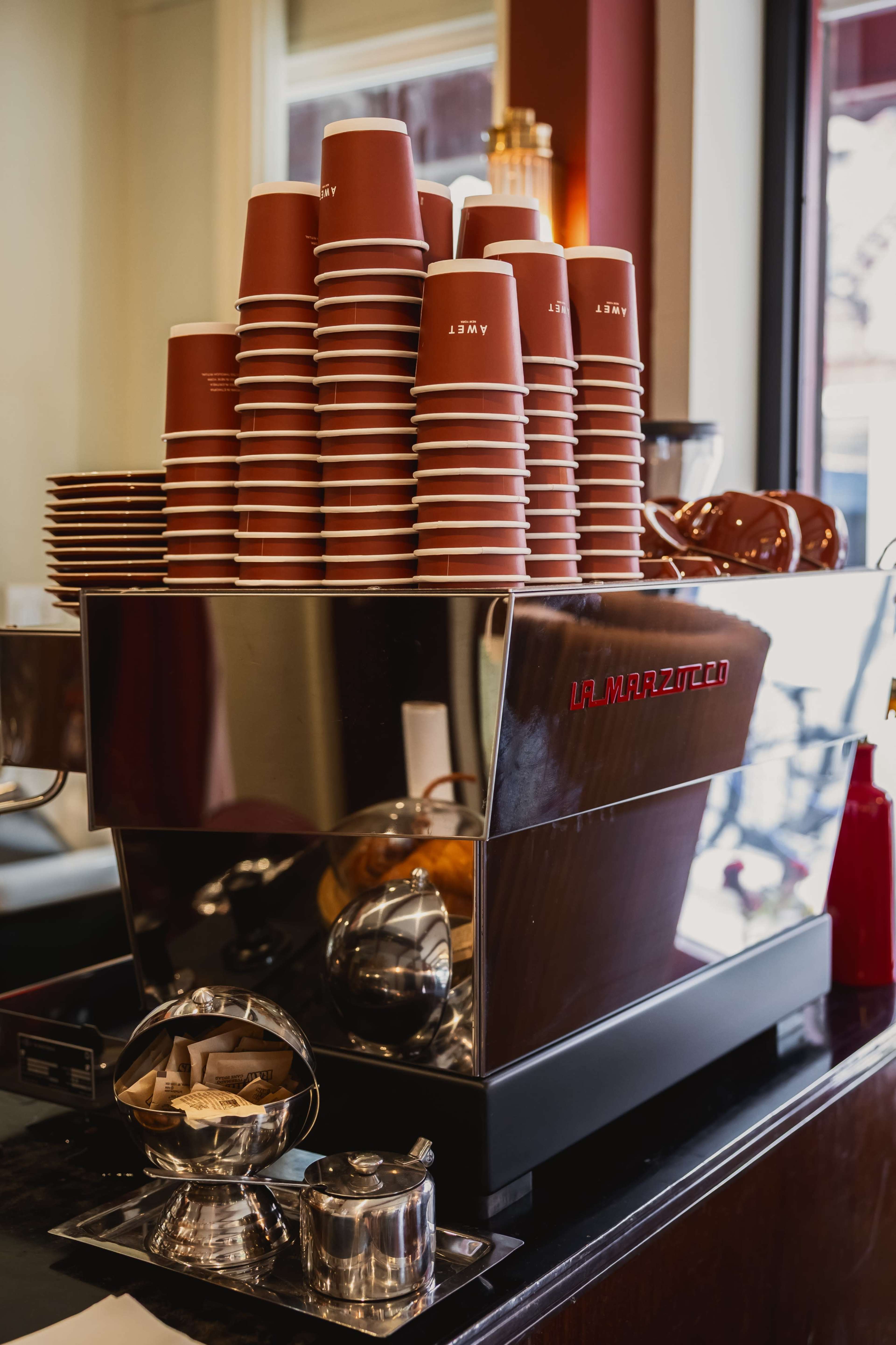 A coffee machine is prominently displayed on a countertop with a stack of red disposable cups beside it.