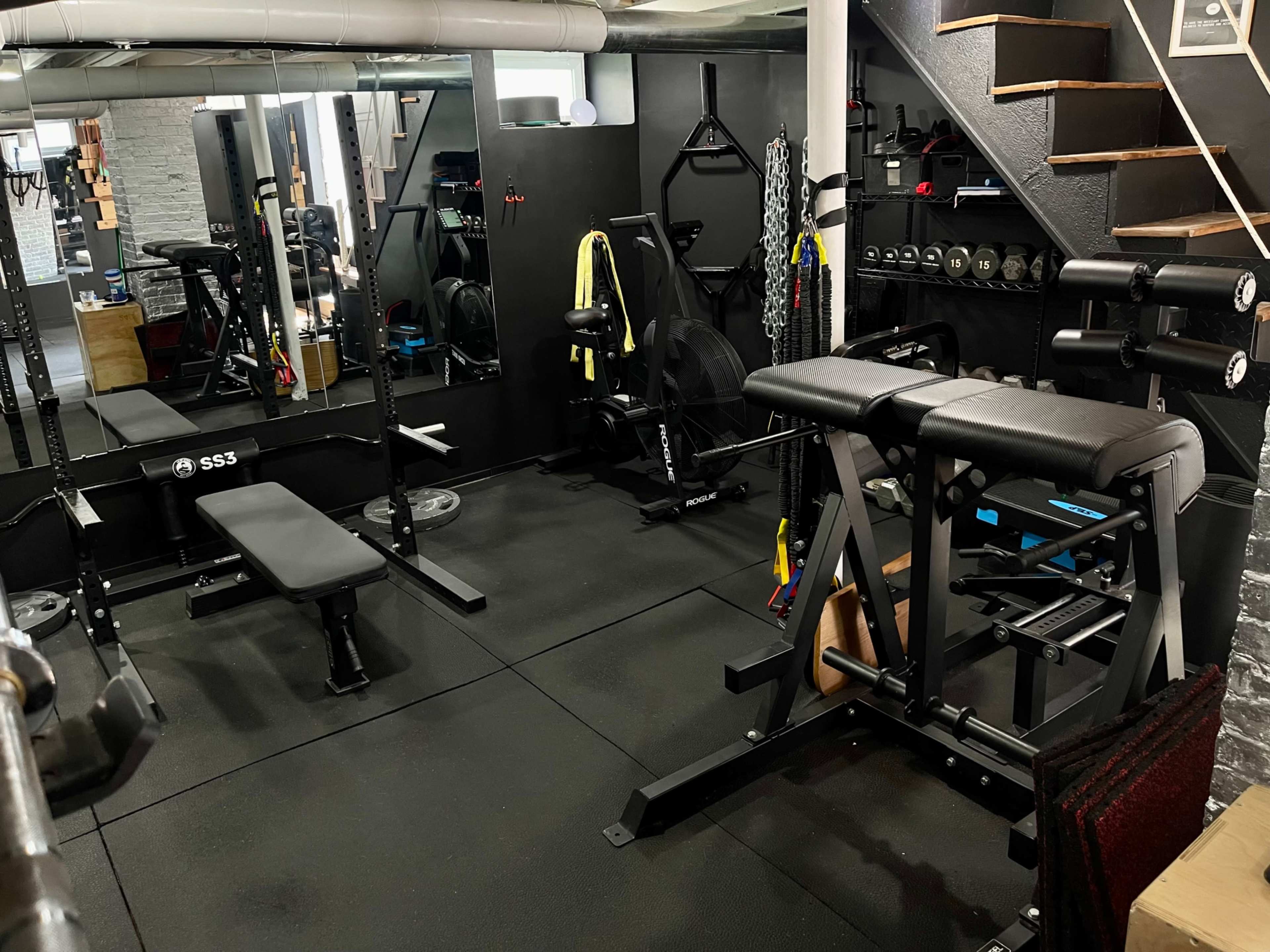 A well-equipped home gym featuring various exercise machines, free weights, and a set of stairs leading to an upper level.