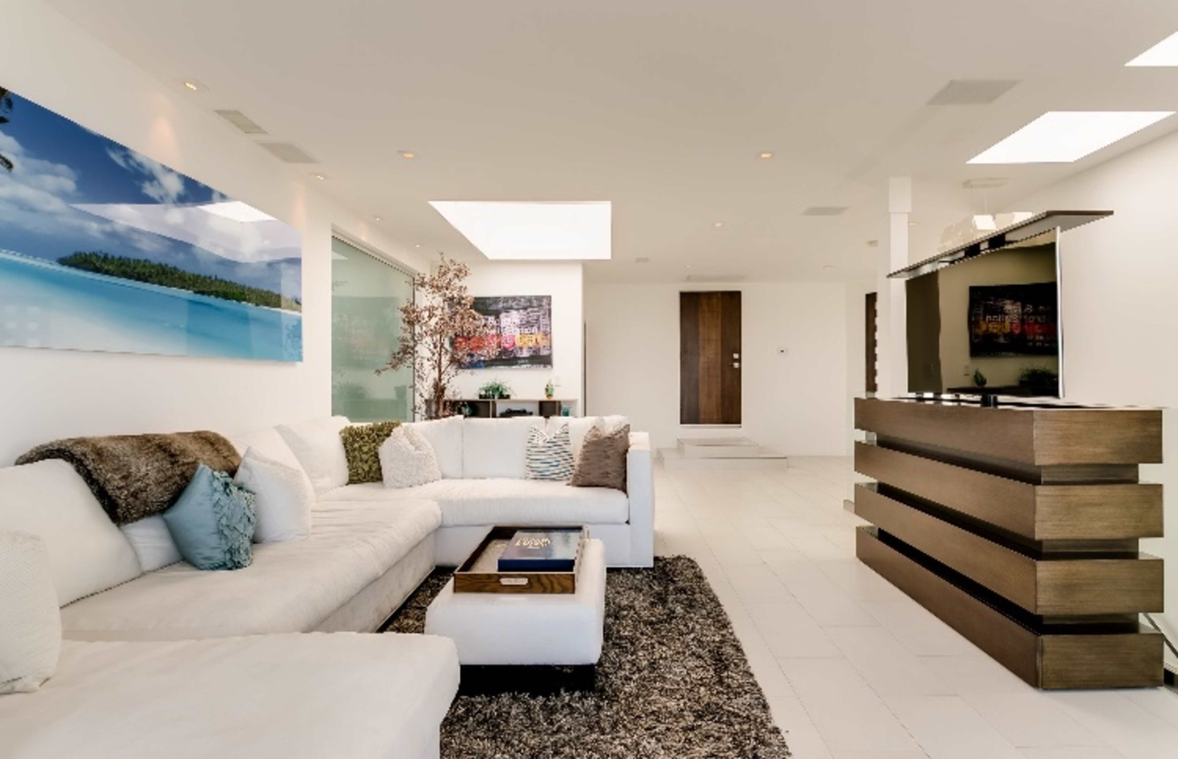 A modern, spacious living room featuring a large white sectional sofa, a dark area rug, and a flat-screen TV mounted on a wooden media console.