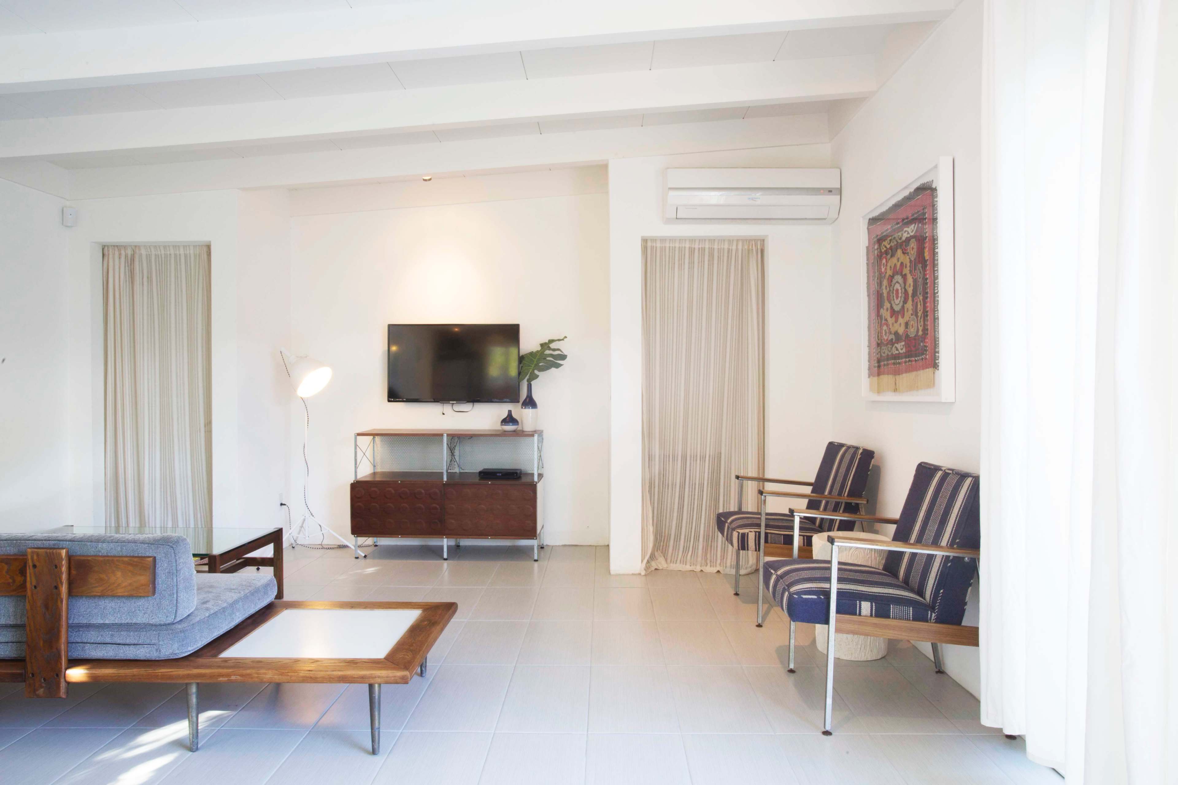 A minimalist living room with a television mounted on the wall, a wooden coffee table, two striped chairs, and a floor lamp.