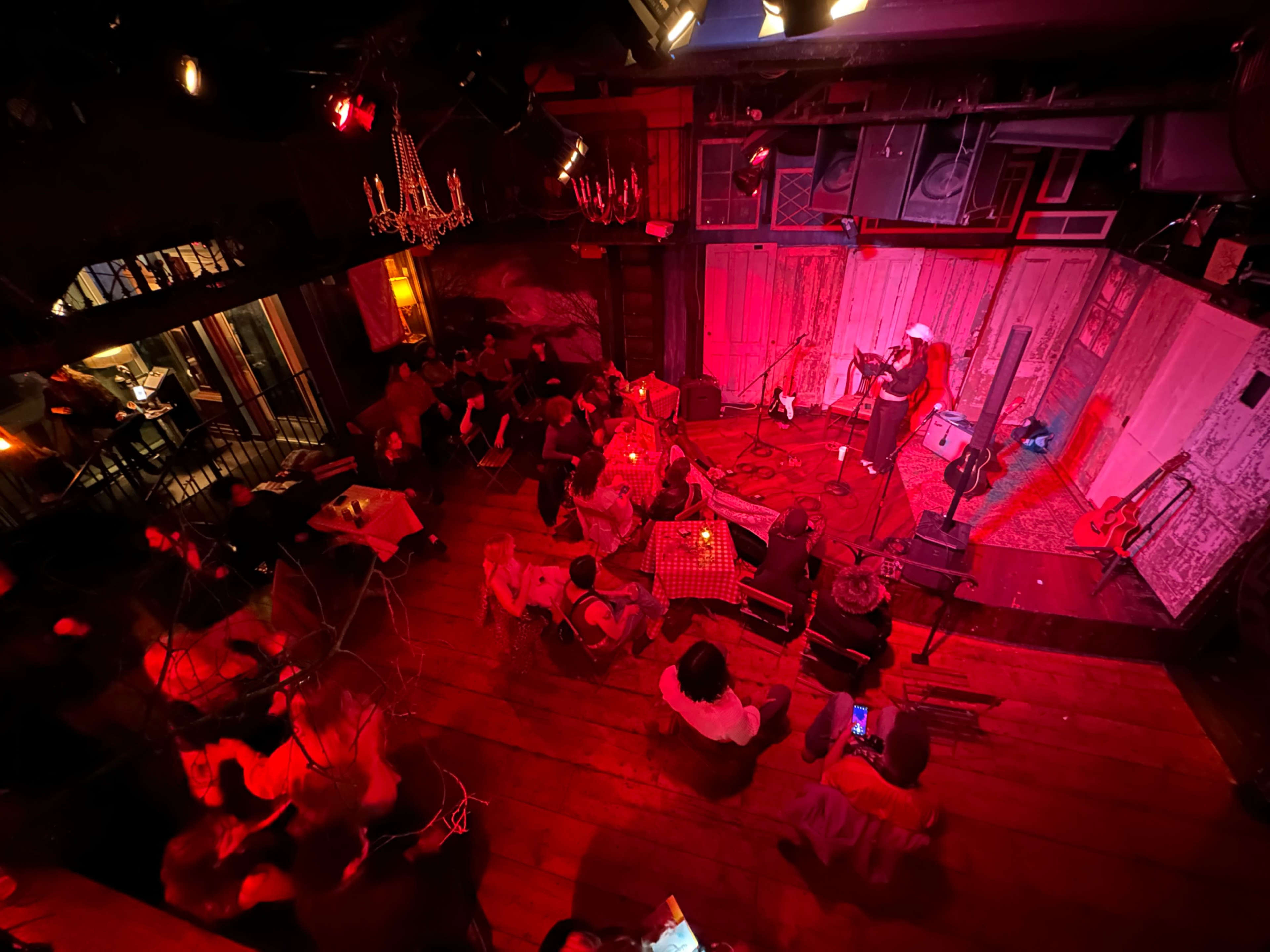 A performer stands on stage in a dimly lit venue filled with seated audience members.