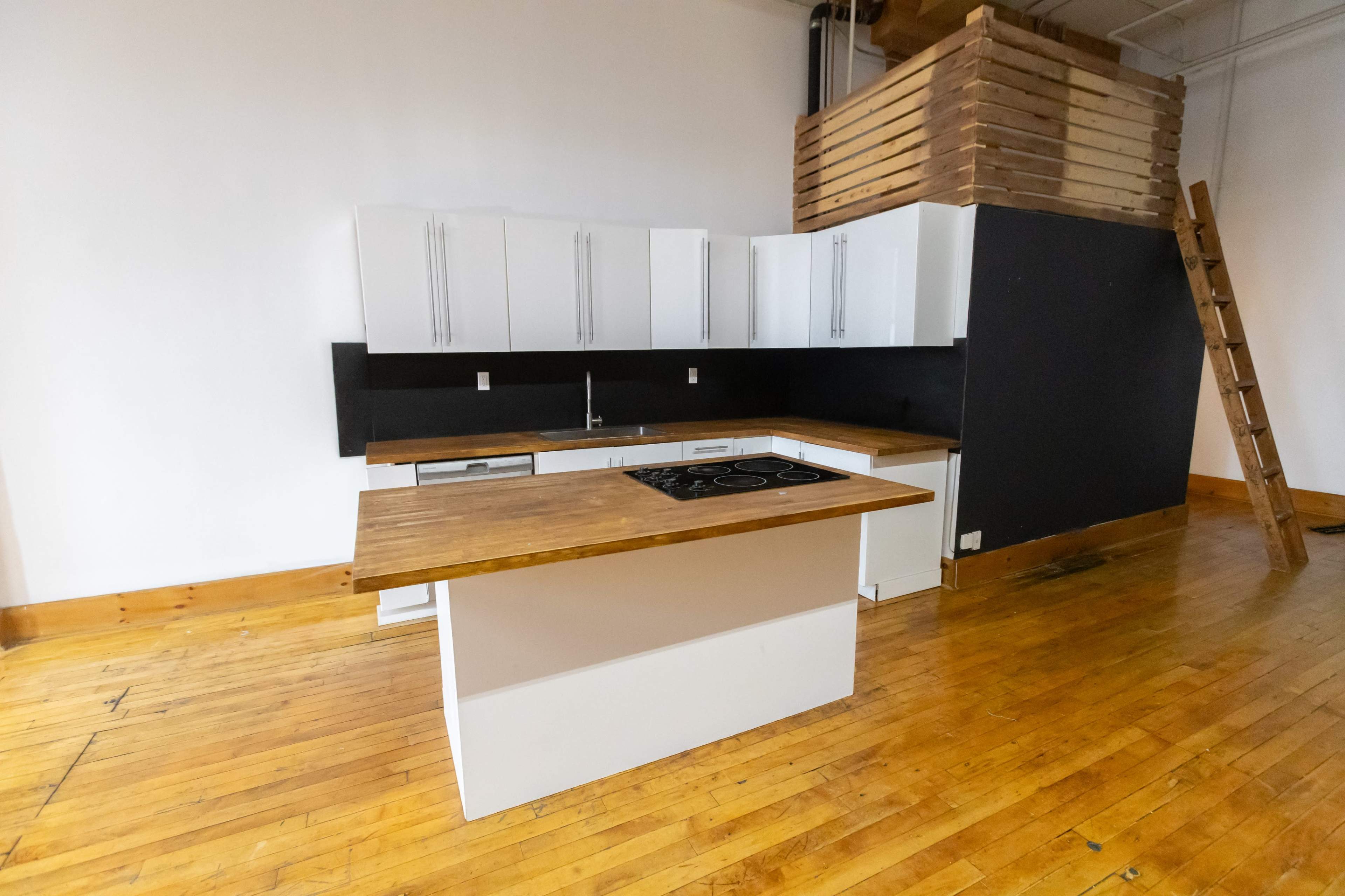 The image shows a modern kitchen with a central island, white cabinetry, a black accent wall, and hardwood flooring.