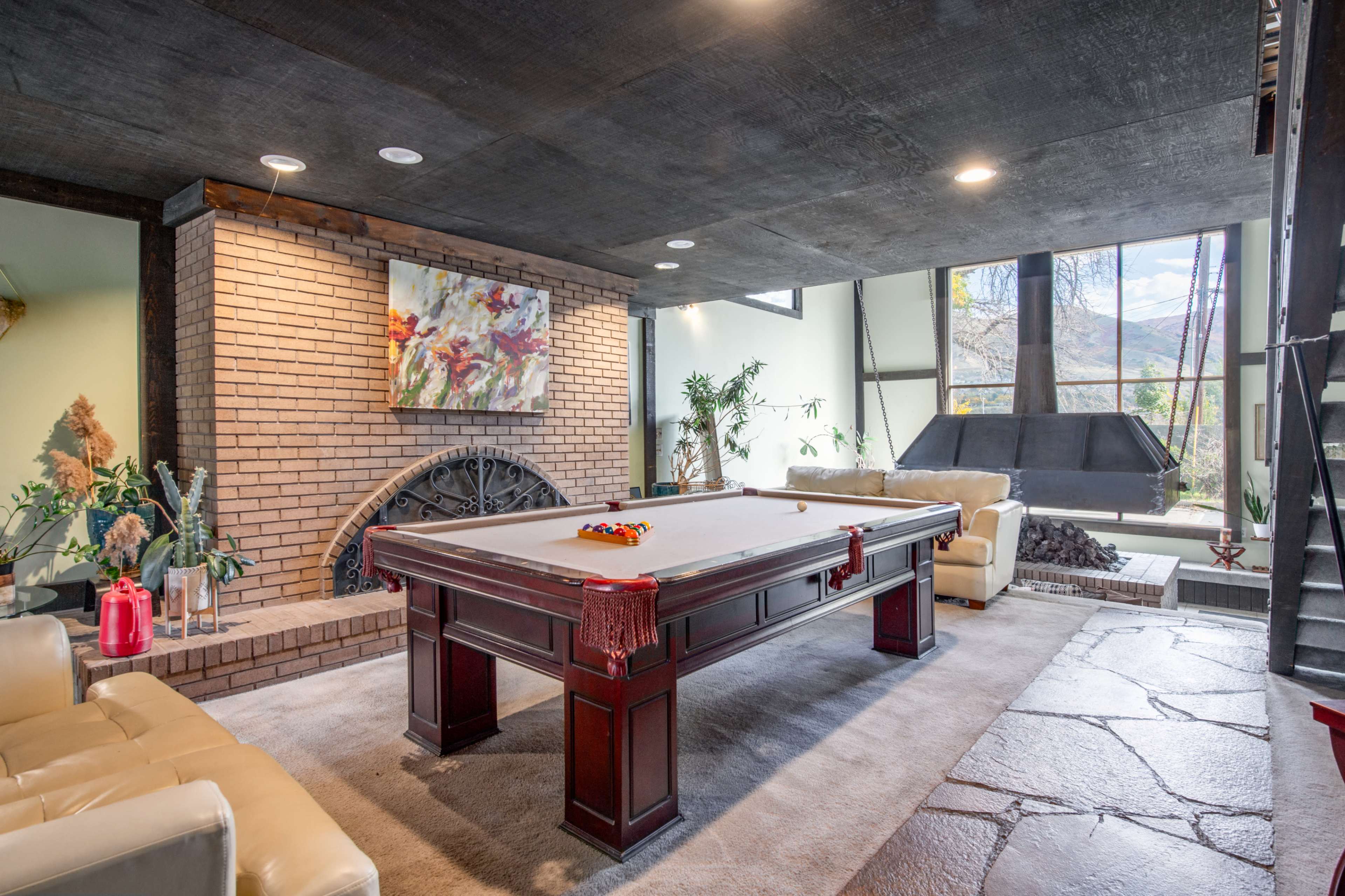 A spacious game room featuring a billiard table, two beige couches, and a brick wall with a large artwork above.