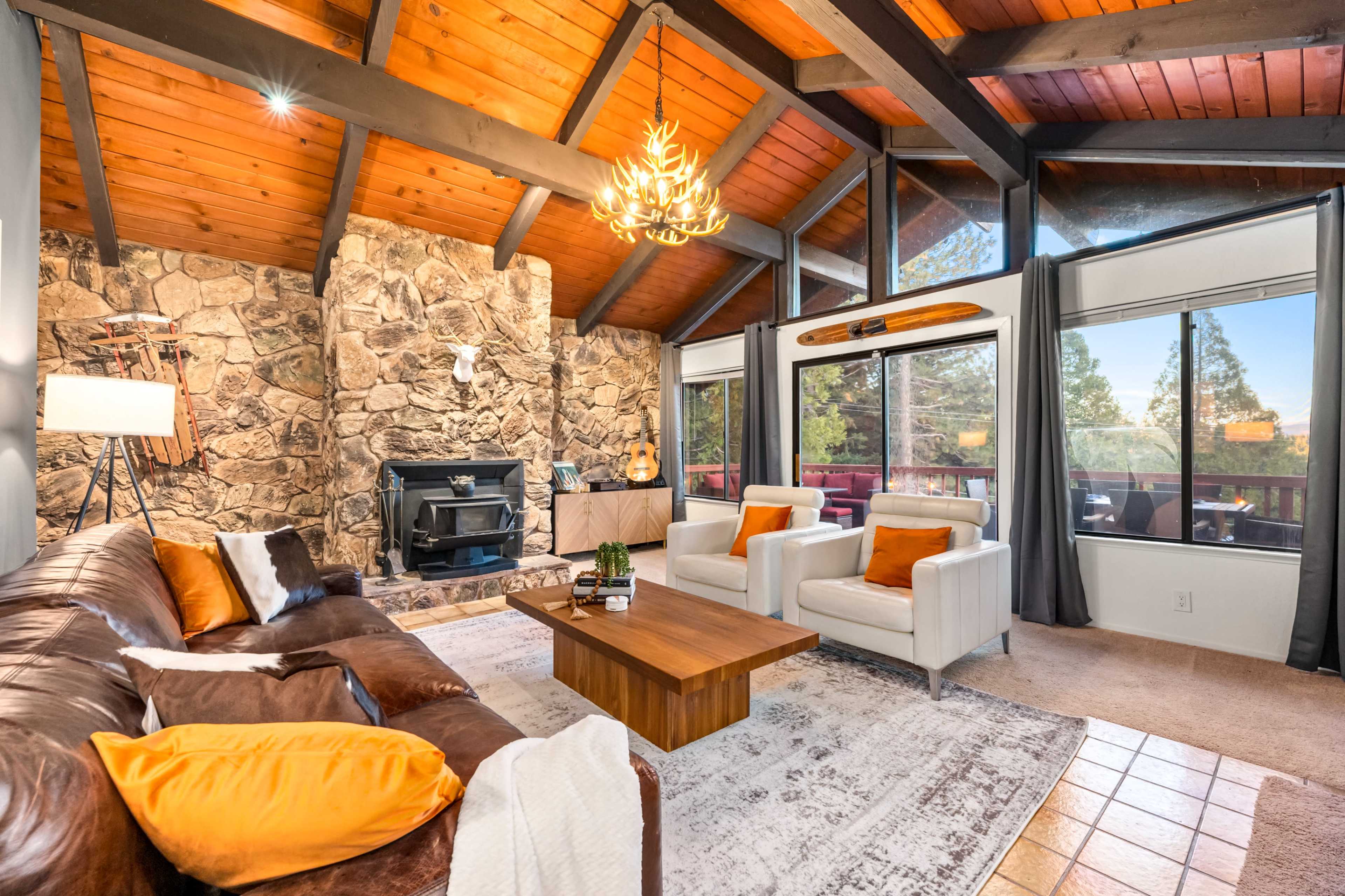 The living room features a stone fireplace, large windows, wooden beams, and leather and upholstered furniture.