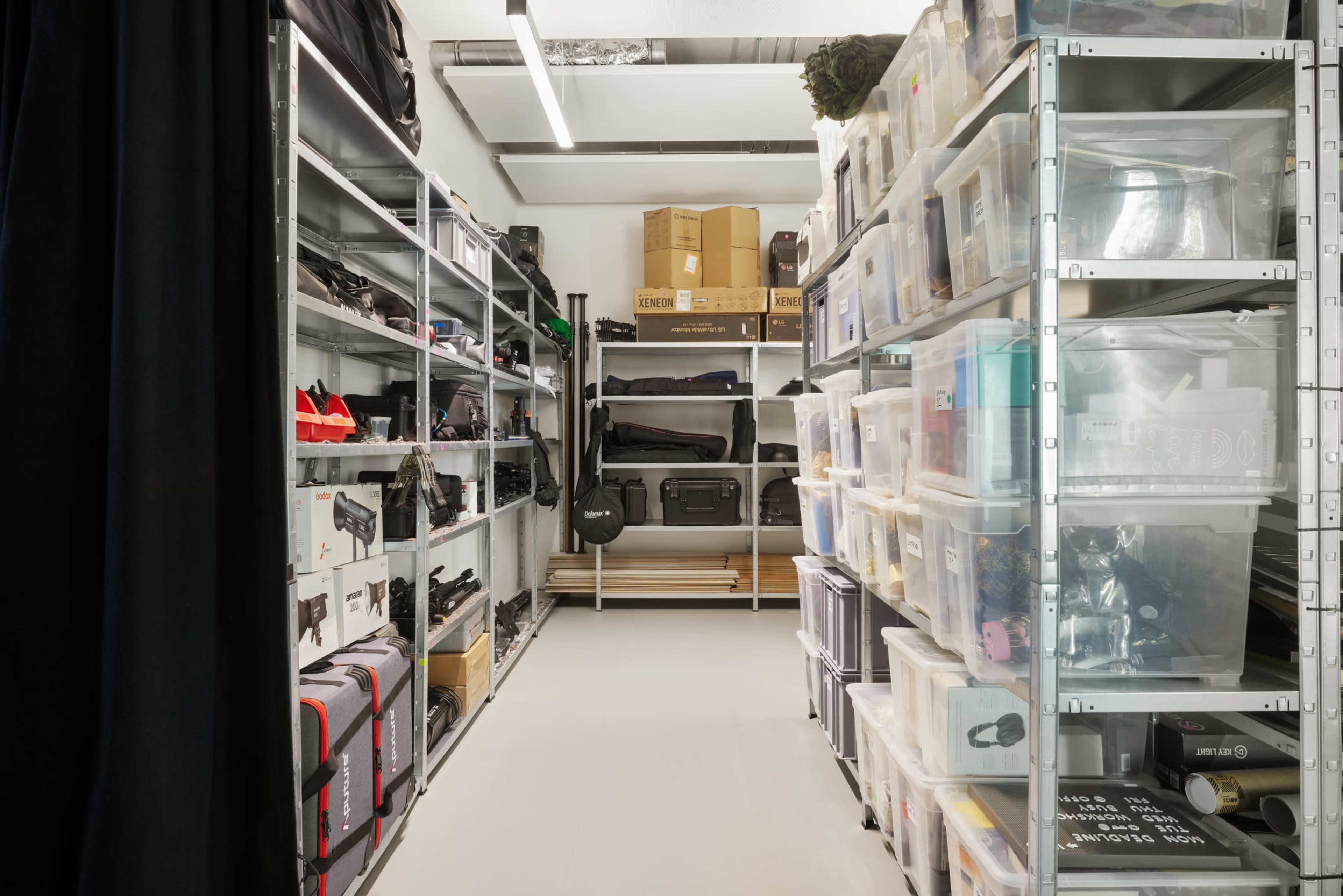 The image shows a neatly organized storage room with metal shelving units filled with boxes, bags, and various equipment.
