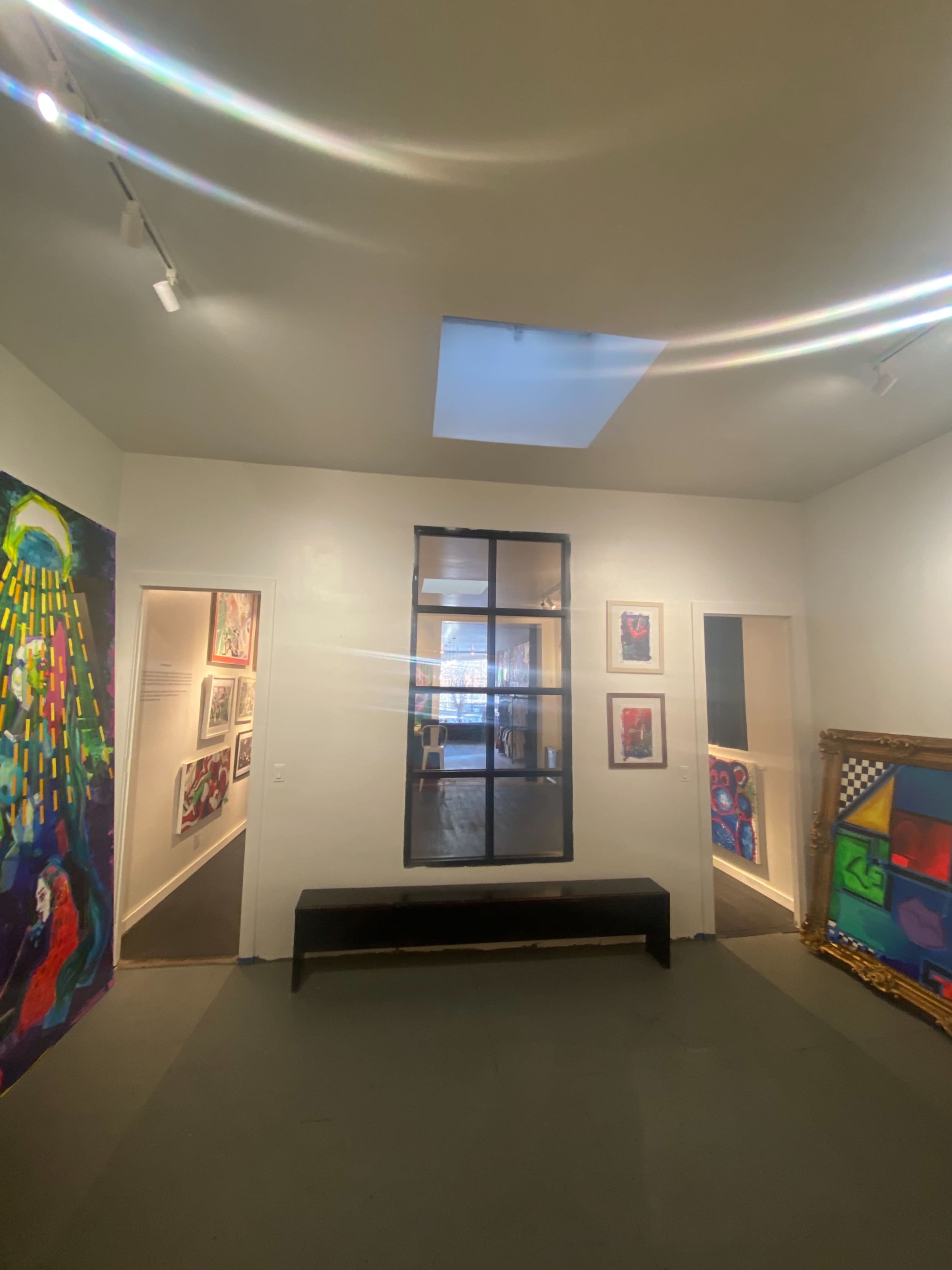 The image shows an art gallery interior with two doorways, colorful paintings on the walls, and a skylight above.