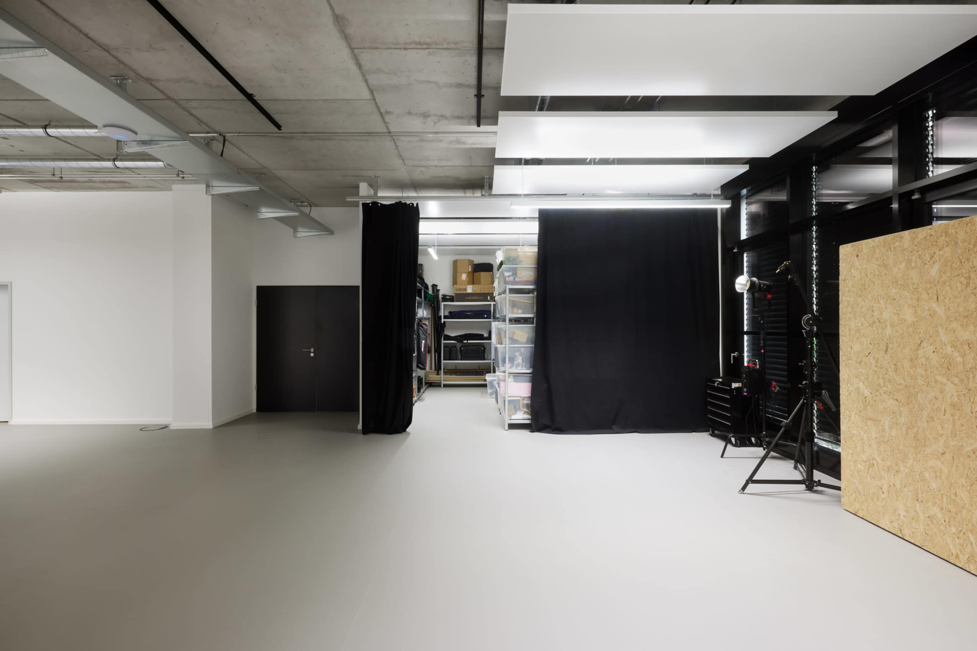 An empty, modern room with a smooth floor, a dark curtain, and storage shelves in the background.